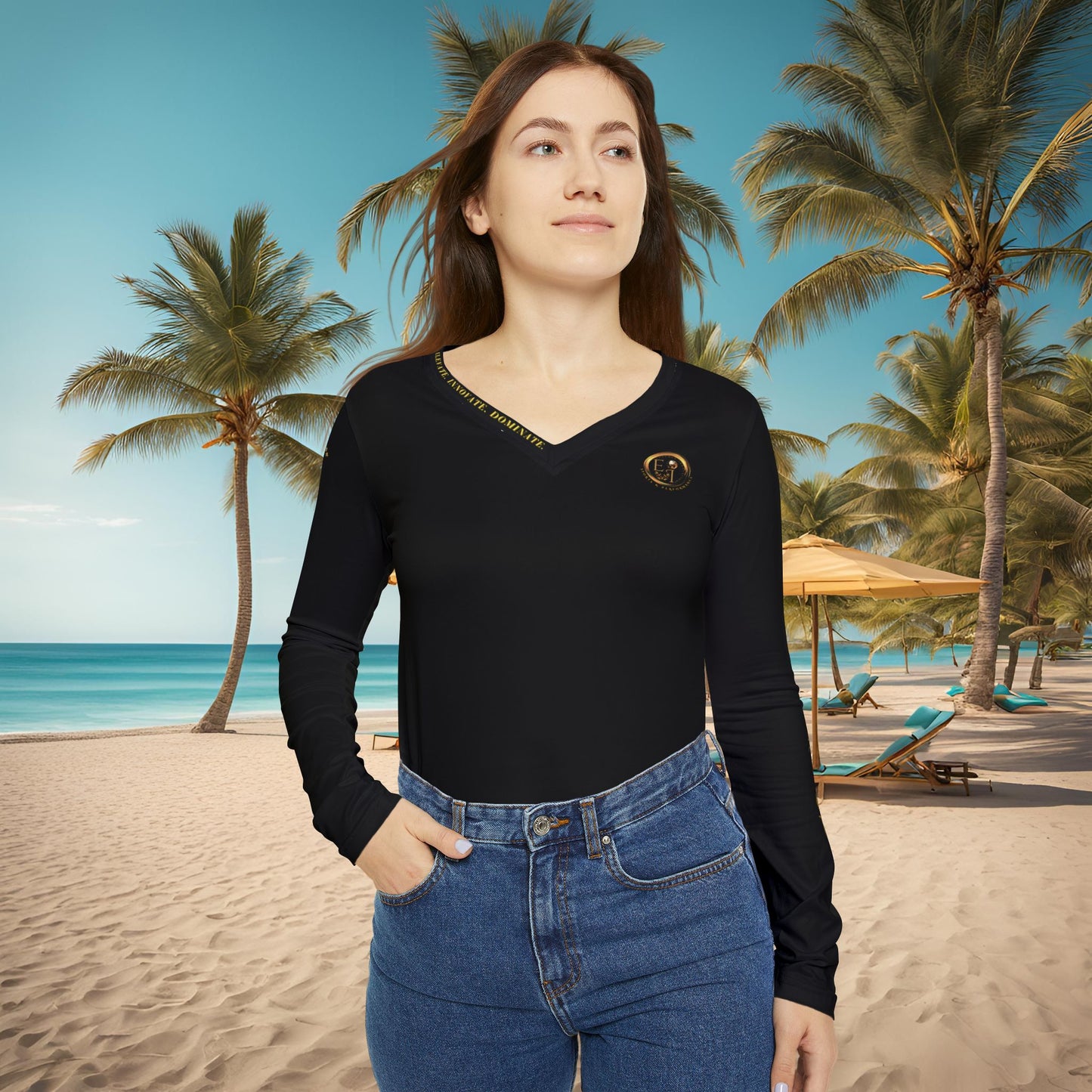 Woman wearing a black Essence Innovation Seek More long-sleeve top and blue jeans on a beach with palm trees and a clear sky.
