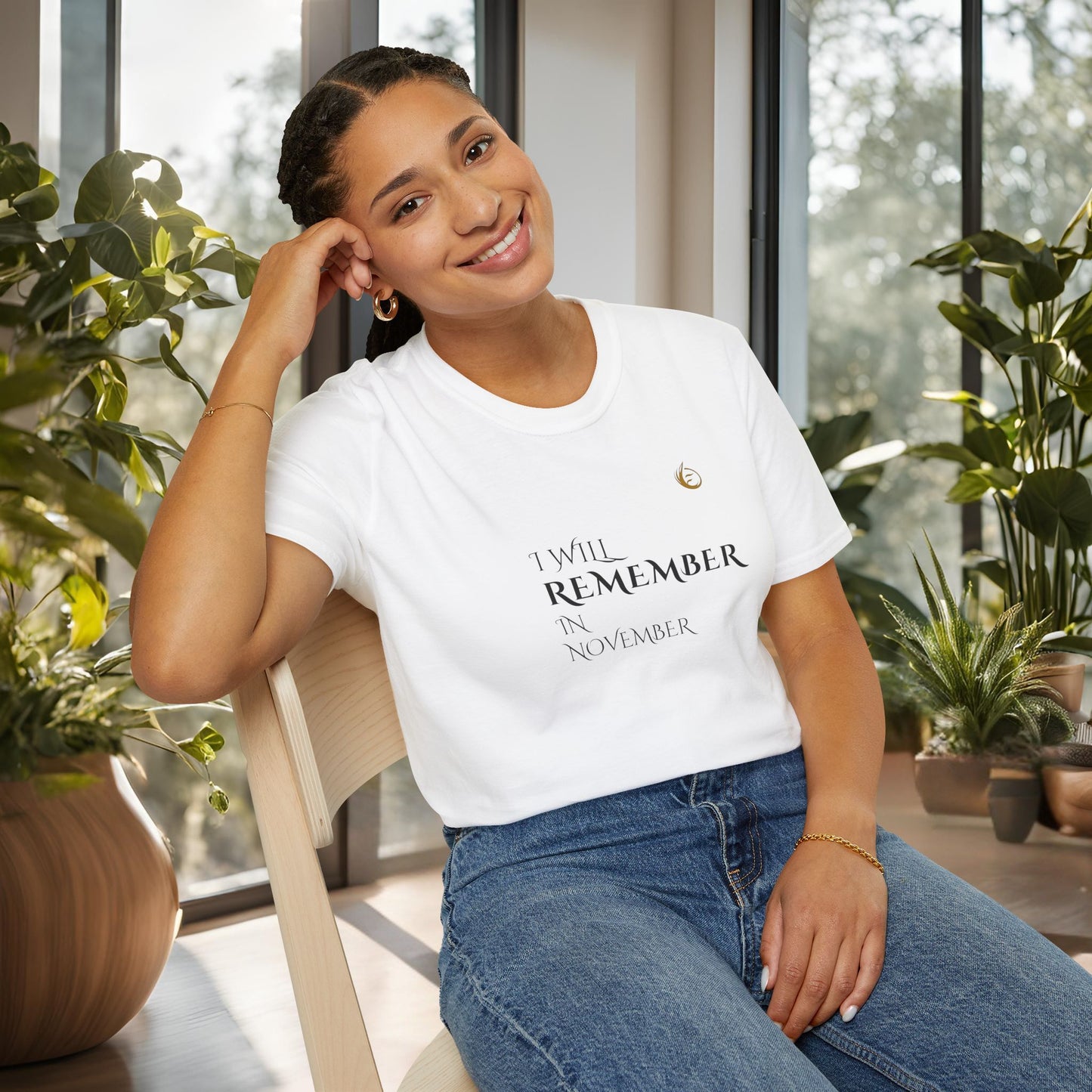 Woman wearing a white EssenceInnoCreate Quiet Resolve t-shirt with text, sitting indoors with plants around.