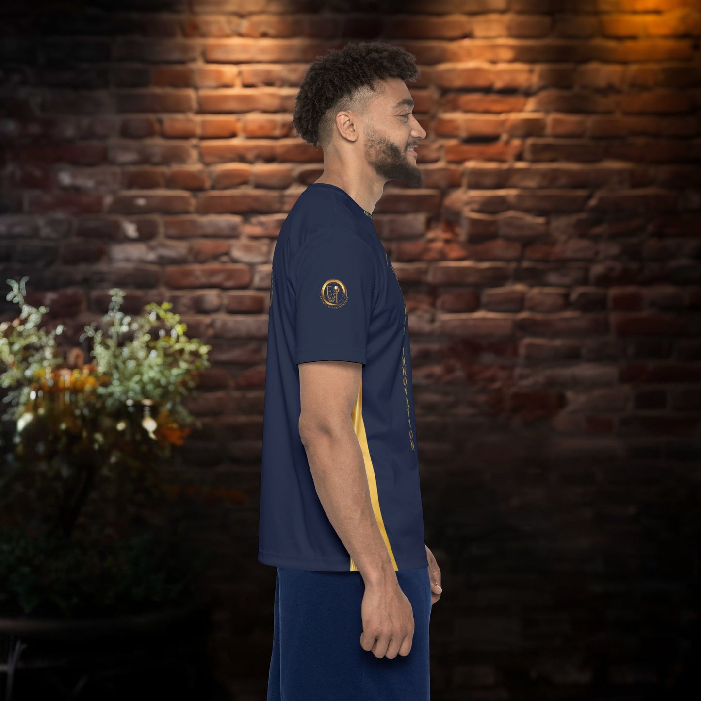 Man wearing a blue sports outfit with a yellow stripe against a brick wall.
