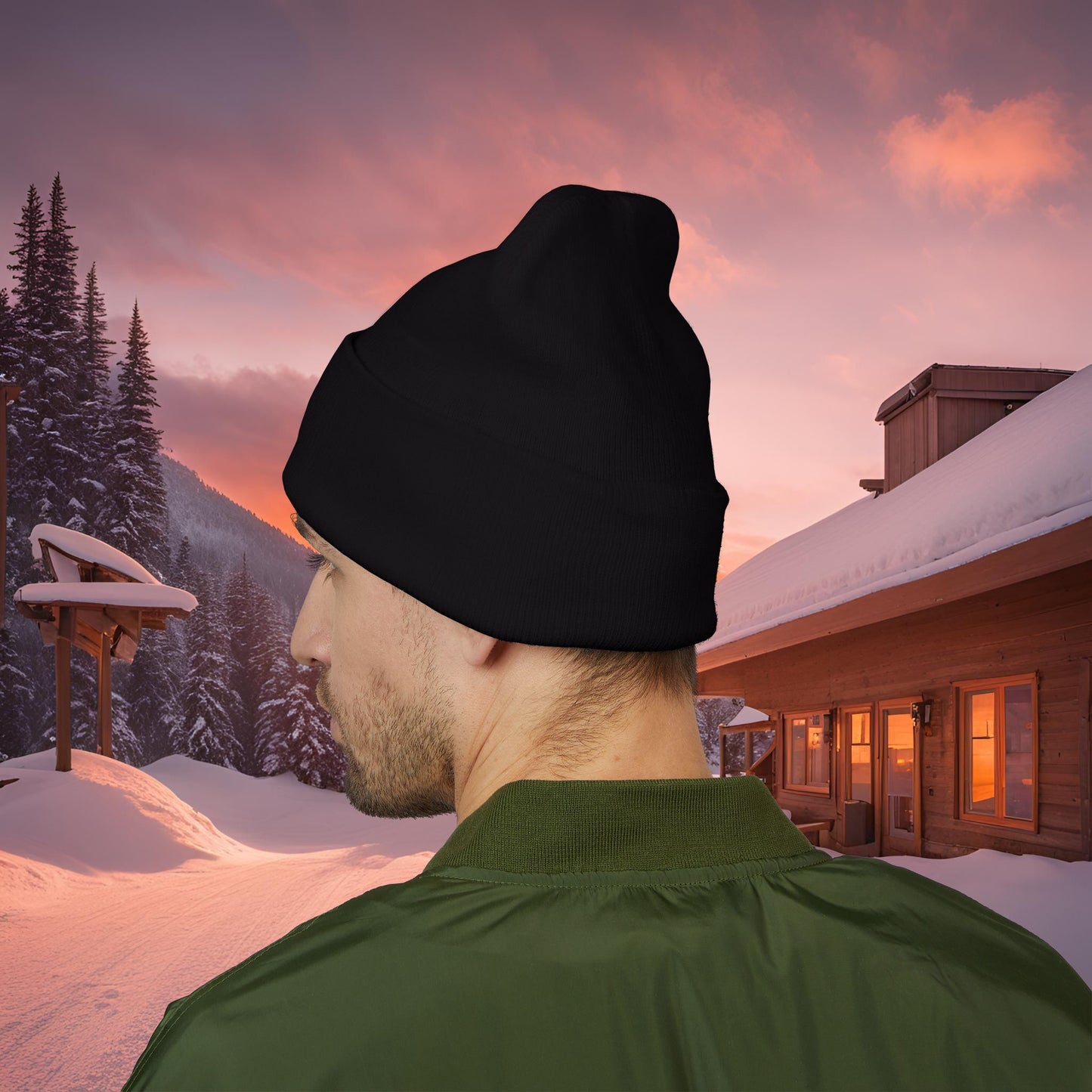 Person wearing a black EssenceInnoCreate beanie and green jacket in a snowy landscape with a cabin and sunset sky.