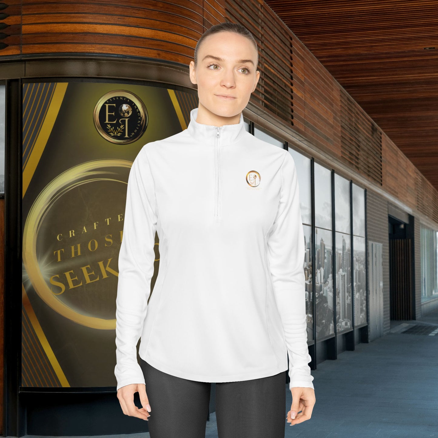 Person wearing a white Essence Innovation Seek More quarter-zip with a logo in front of a building entrance