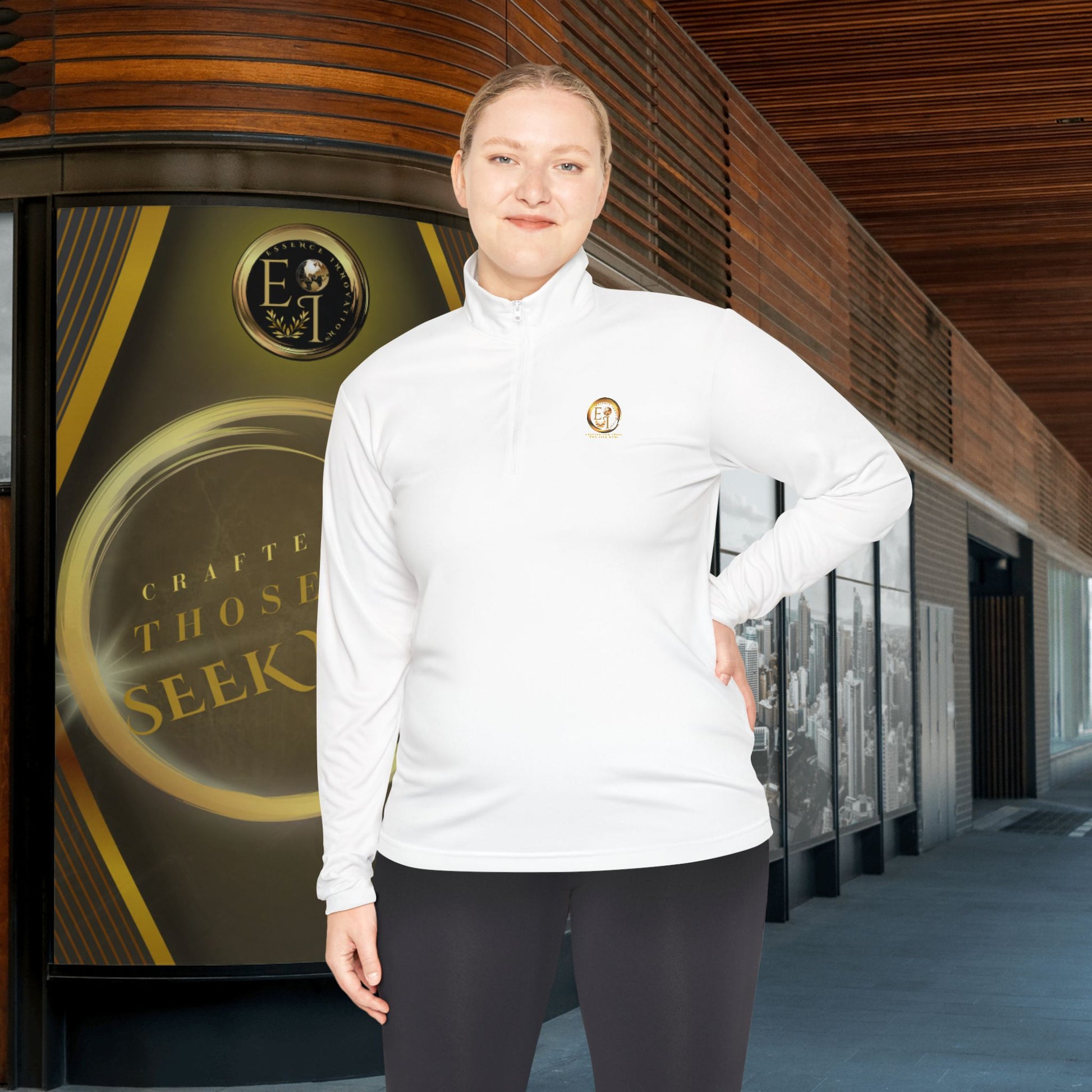 Person wearing a white Essence Innovation Seek More quarter-zip with a logo in front of a building with a large sign.