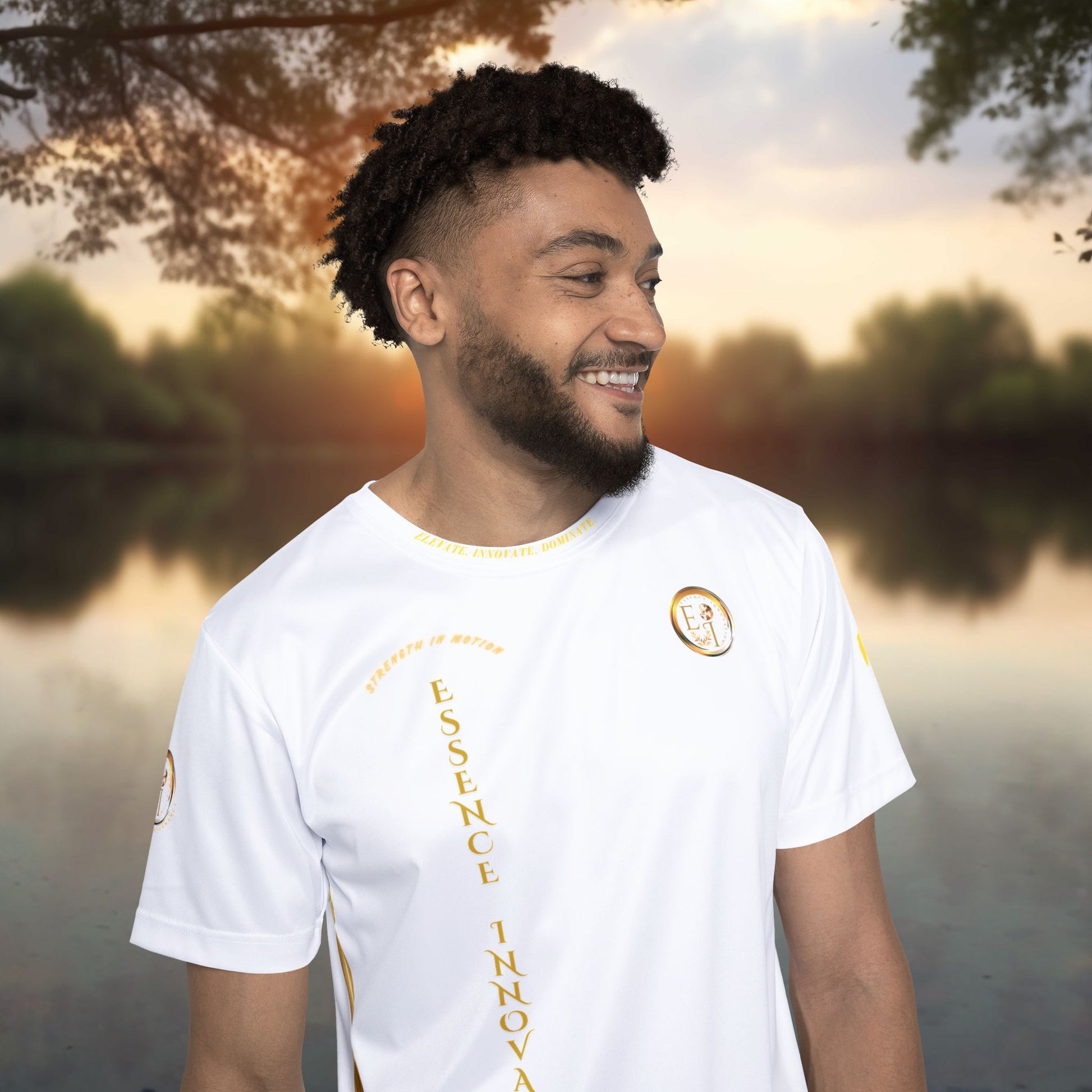 Man wearing a white t-shirt with gold Essence Innovation text and design, standing outdoors with a blurred natural background
