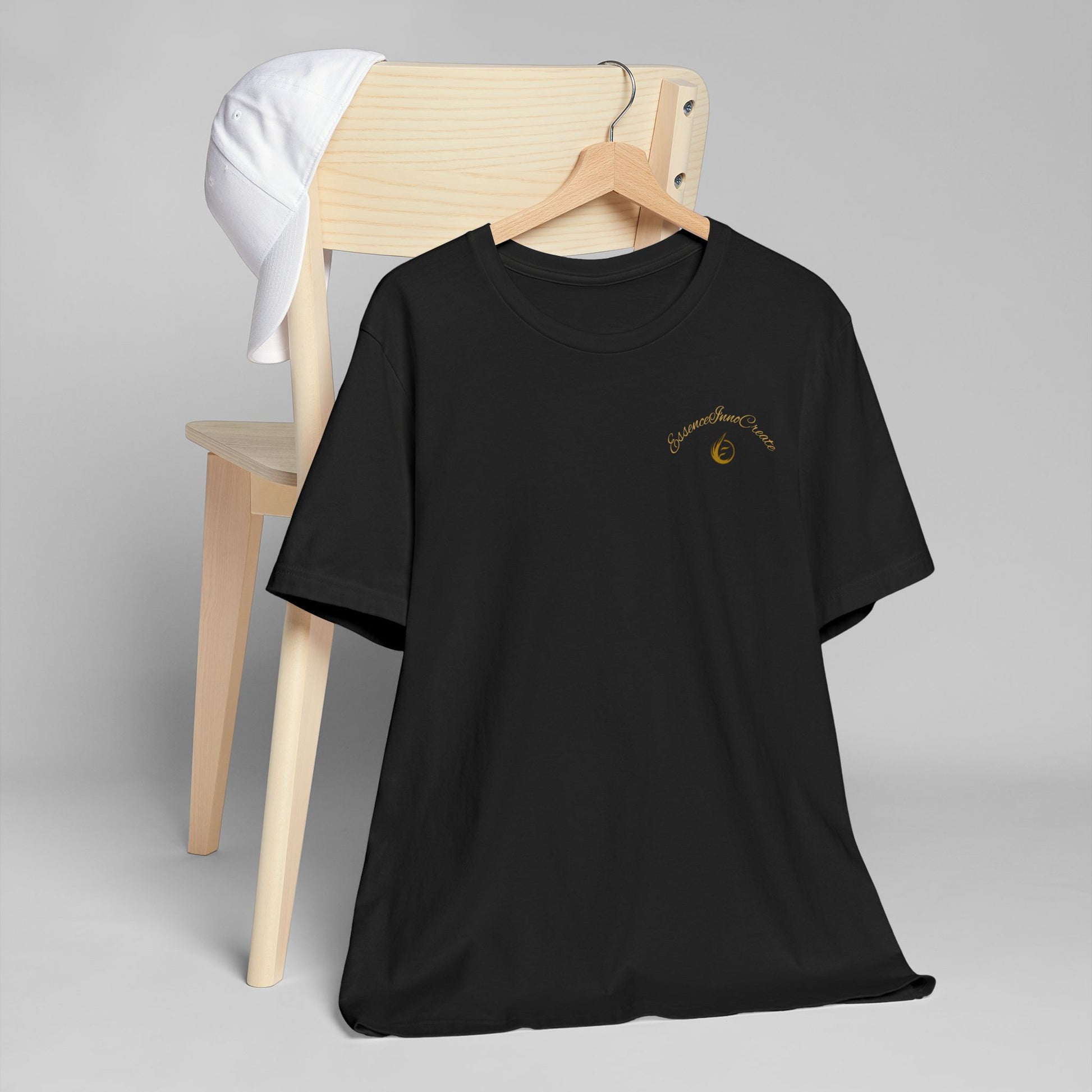 Black t-shirt with a graphic 'EssenceInnoCreate' design on a wooden chair against a gray background