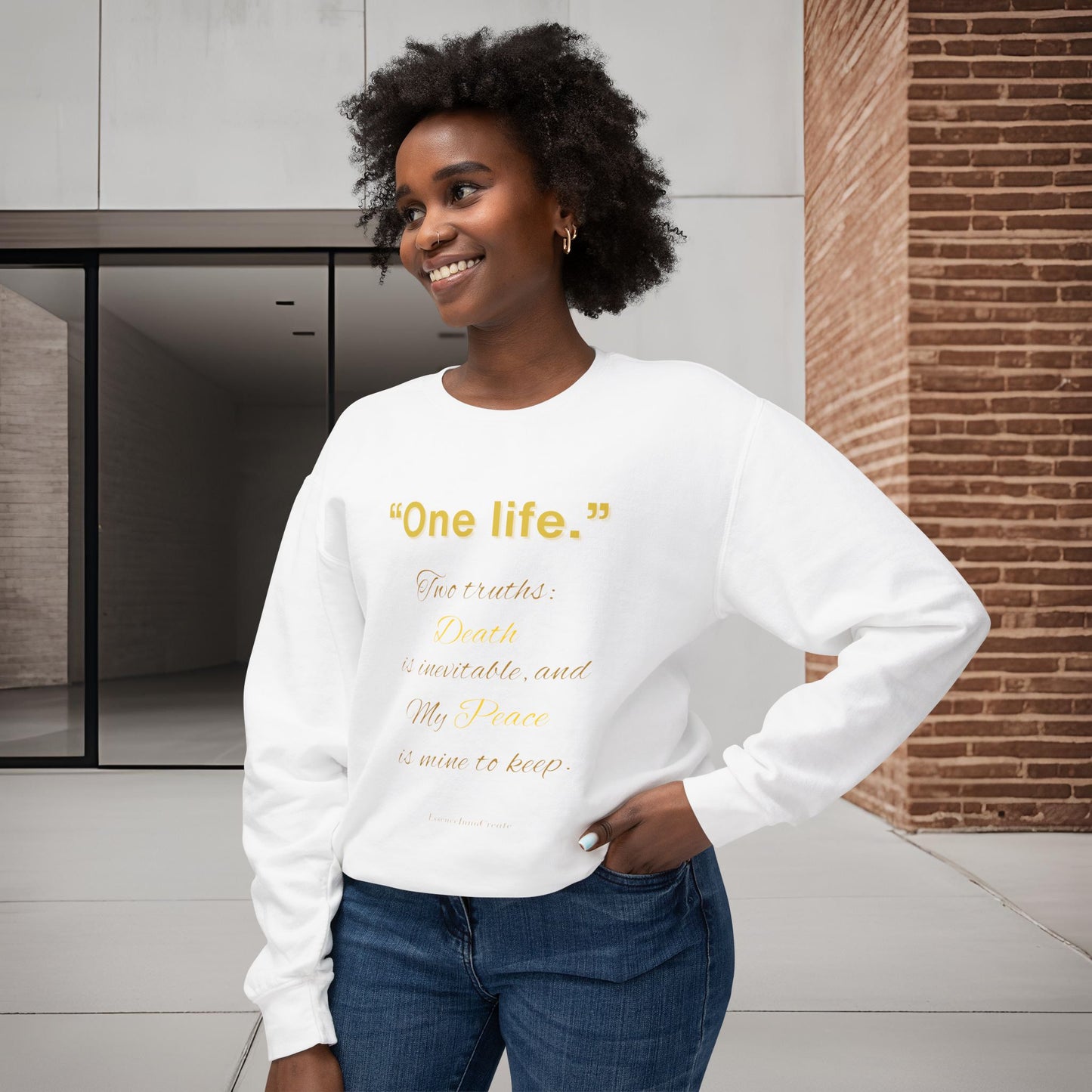 Woman wearing a white sweatshirt with yellow One Life text standing in a modern indoor setting.