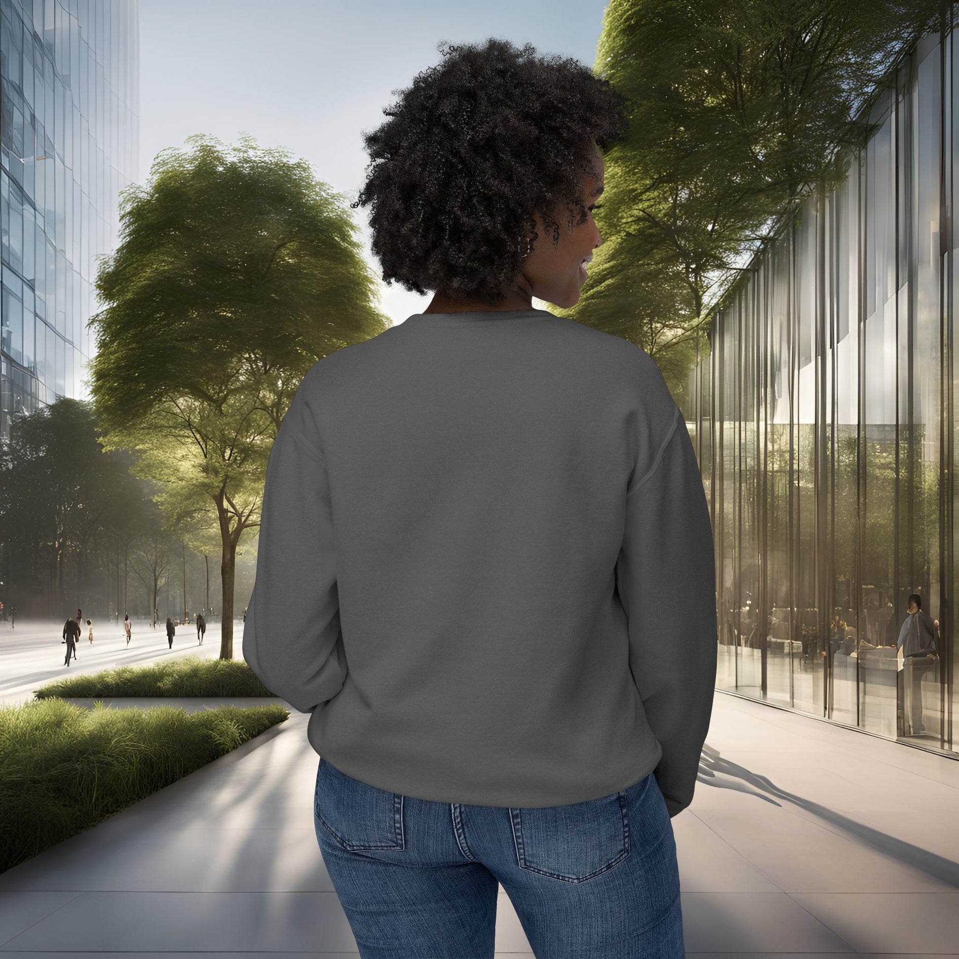 Person wearing a gray sweatshirt and blue jeans standing on a sidewalk with modern buildings and trees in the background.