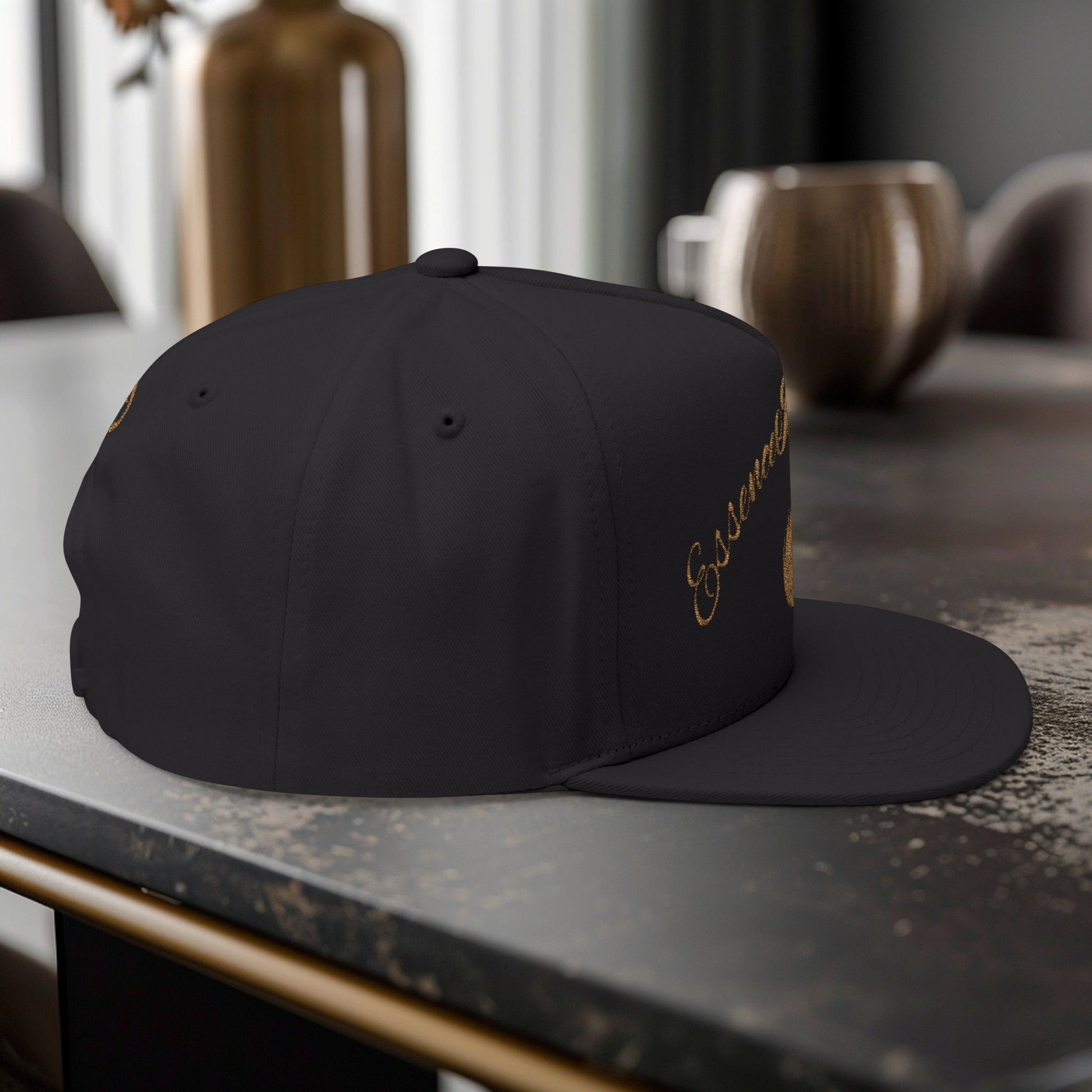 Black cap with gold EssenceInnoCreate embroidery on a dark surface