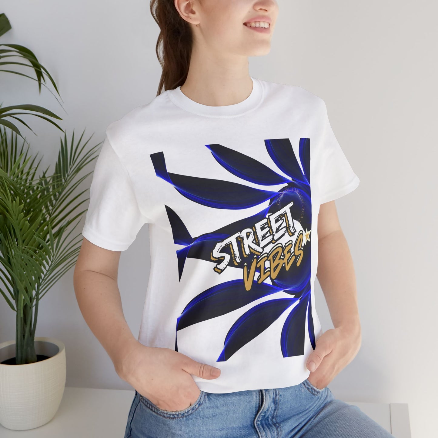 Person wearing a white EssenceInnoCreate t-shirt with 'Street Vibes' design, standing indoors next to a plant.