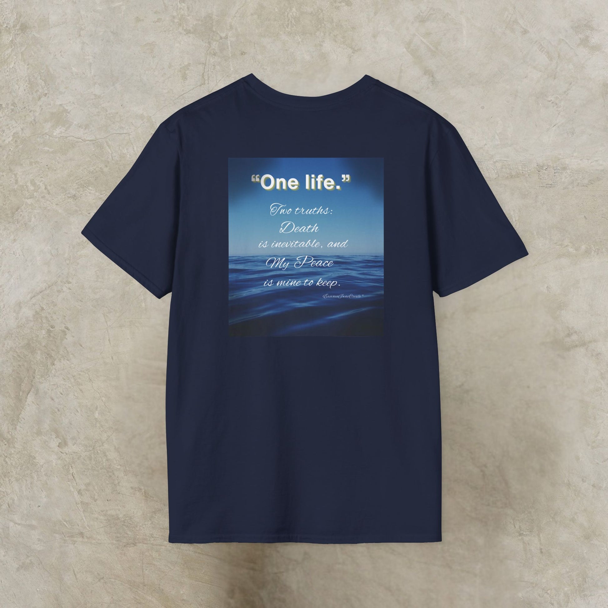 Navy blue t-shirt with a graphic and One Life text on the back, displayed on a textured beige surface.