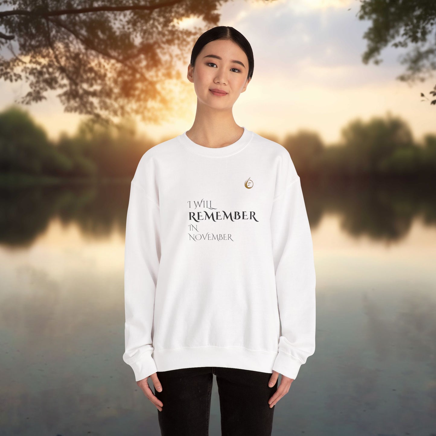 Person wearing a white EssenceInnoCreate Quiet Resolve sweatshirt with text standing by a lake at sunset