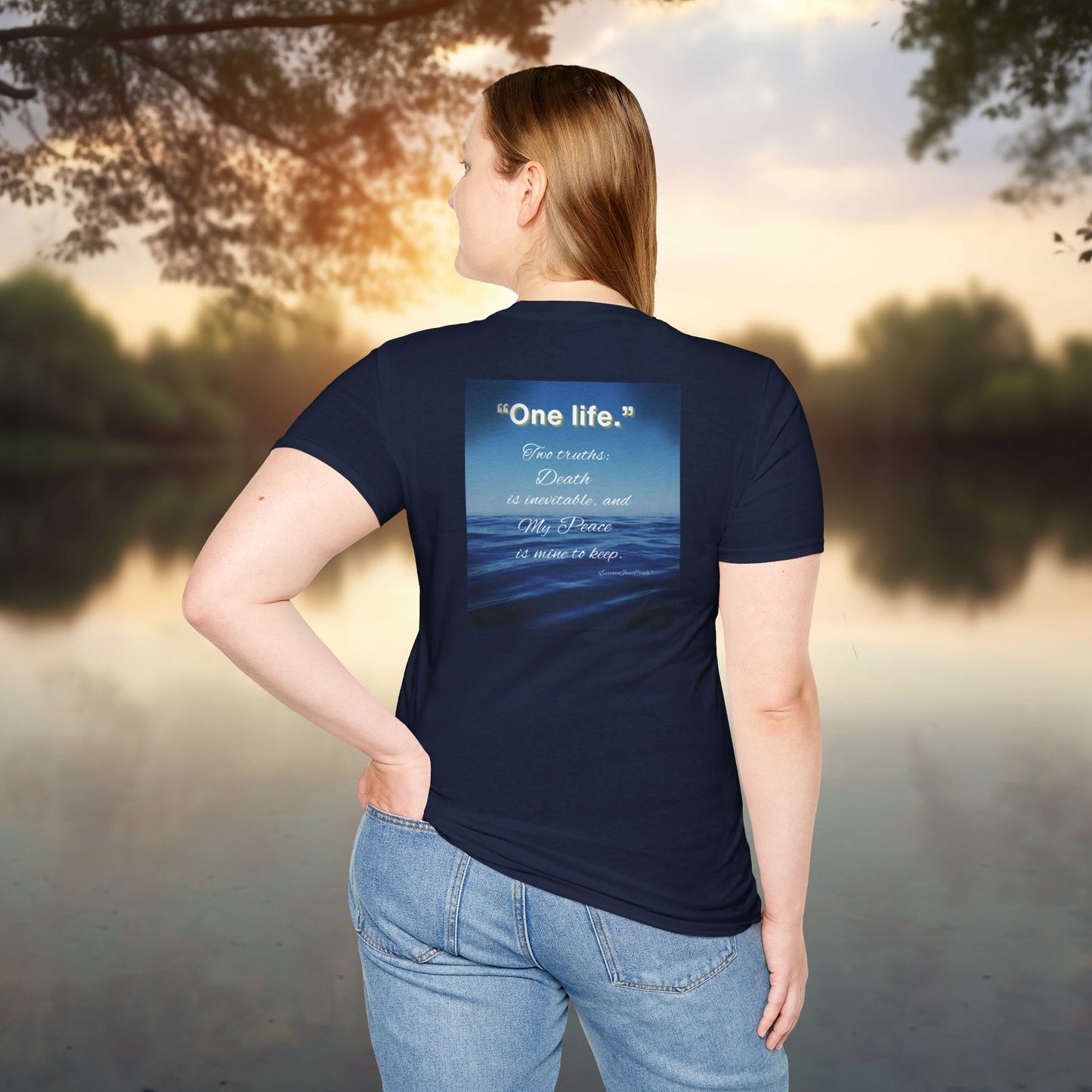 Person wearing a navy blue t-shirt with a One Life quote on the back, standing by a lake at sunset.