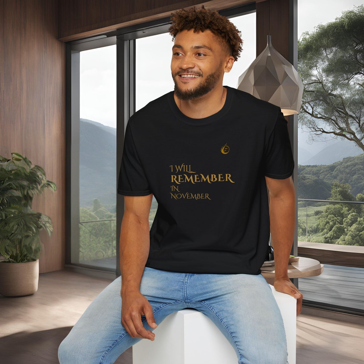 Man wearing a black EssenceInnoCreate Quiet Resolve t-shirt with text, sitting in a modern room with large windows.