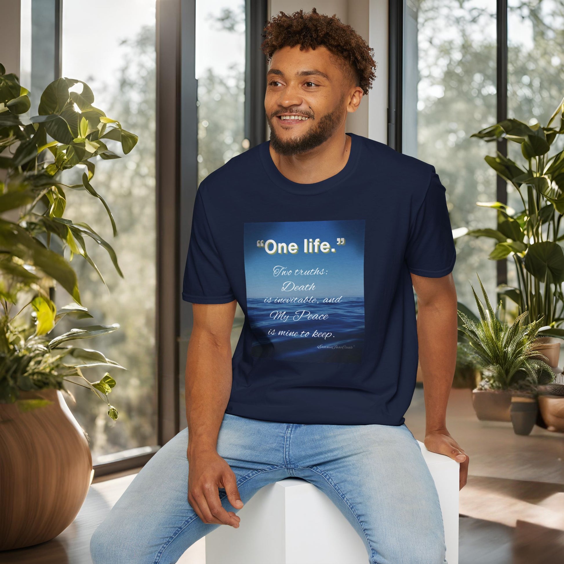 Man wearing a navy blue 'One Life' t-shirt with a quote, sitting in a room with plants.