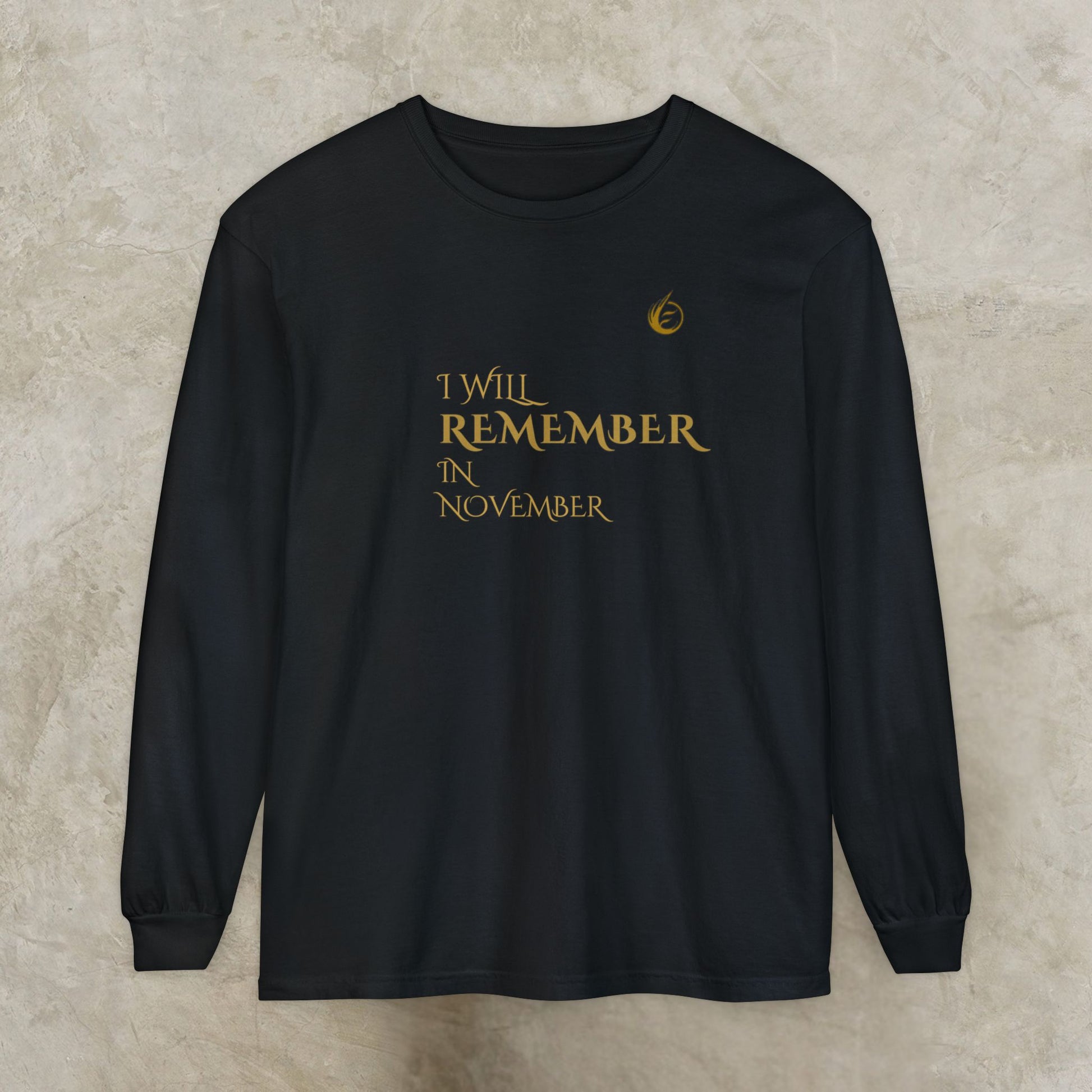 Black long-sleeve EssenceInnoCreate Quiet Resolve shirt with gold text 'I WILL REMEMBER IN NOVEMBER' on a beige background