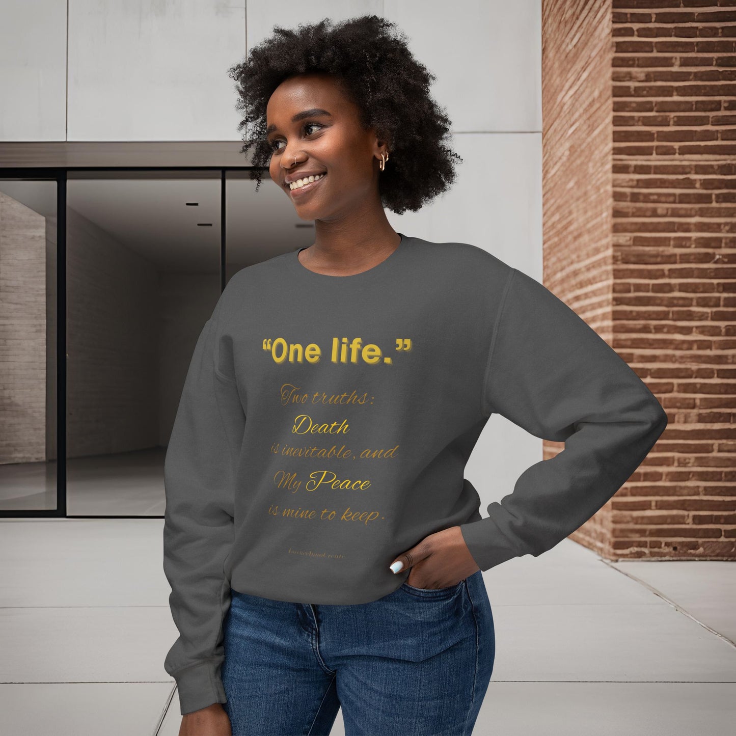 Woman wearing a gray sweatshirt with One Life text, standing in a modern indoor setting.