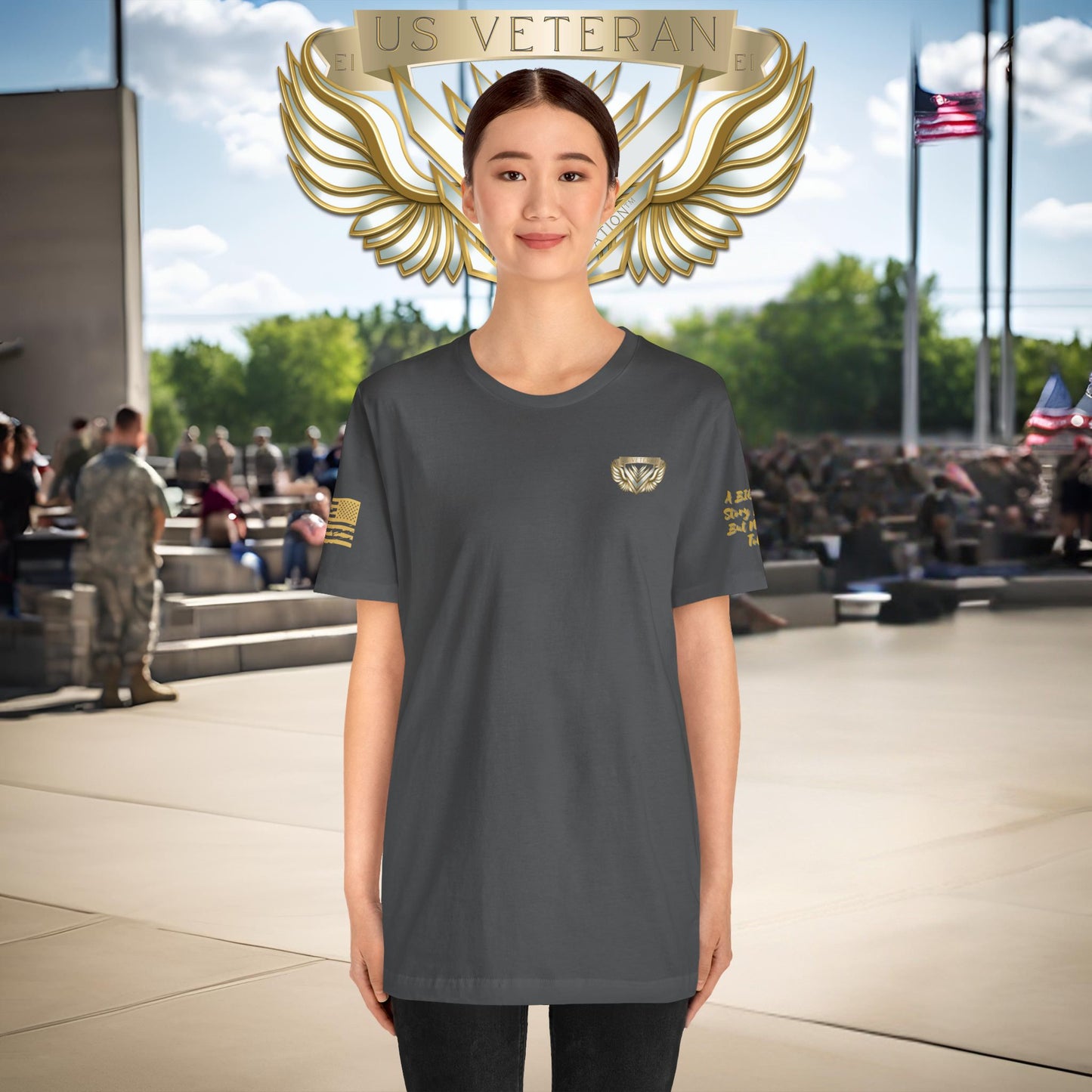 Person wearing a gray t-shirt with a gold emblem, standing in front of a crowd with American flags in the background.