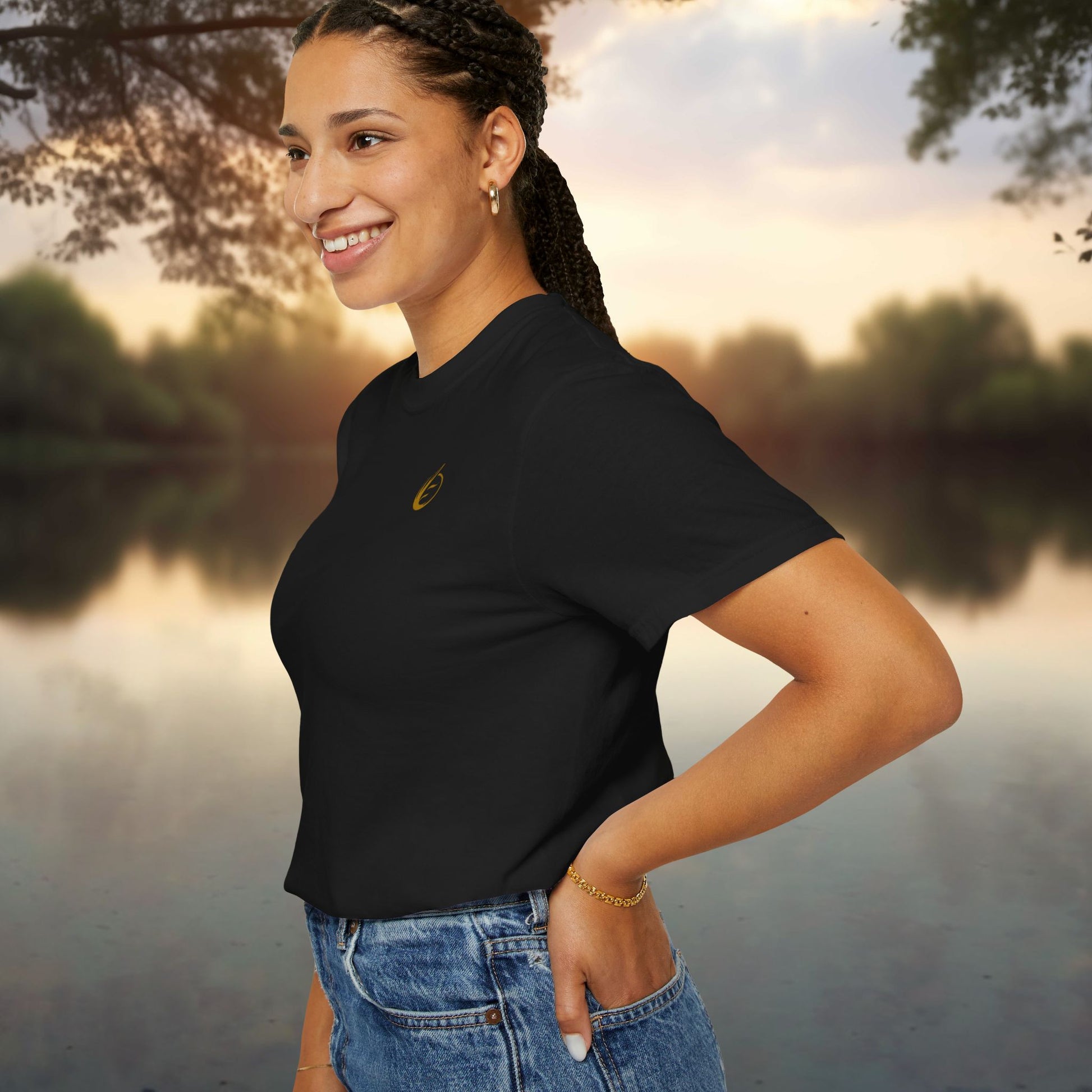 Woman wearing a black t-shirt with 'EssenceInnoCreate' yellow logo by a lake at sunset
