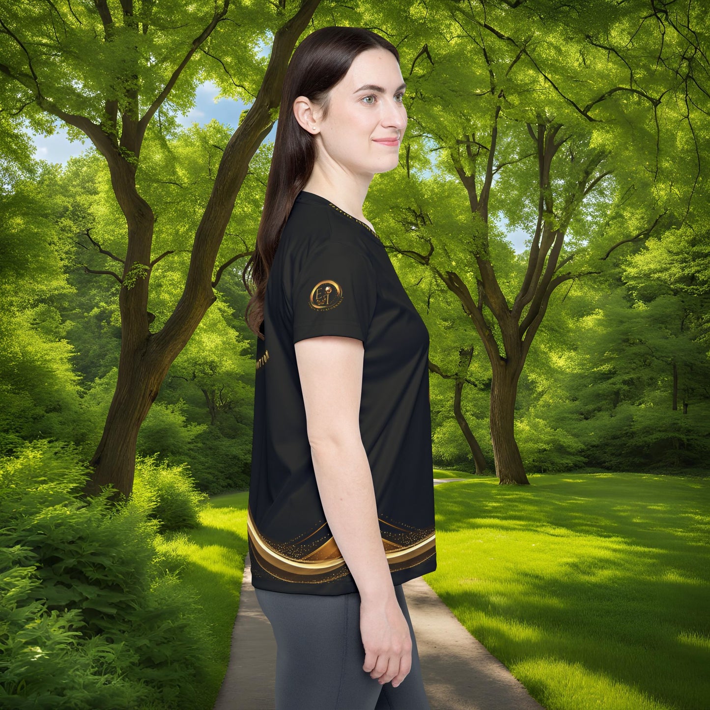 Woman wearing a black t-shirt with gold Essence Innovation Seek More design in a forest setting