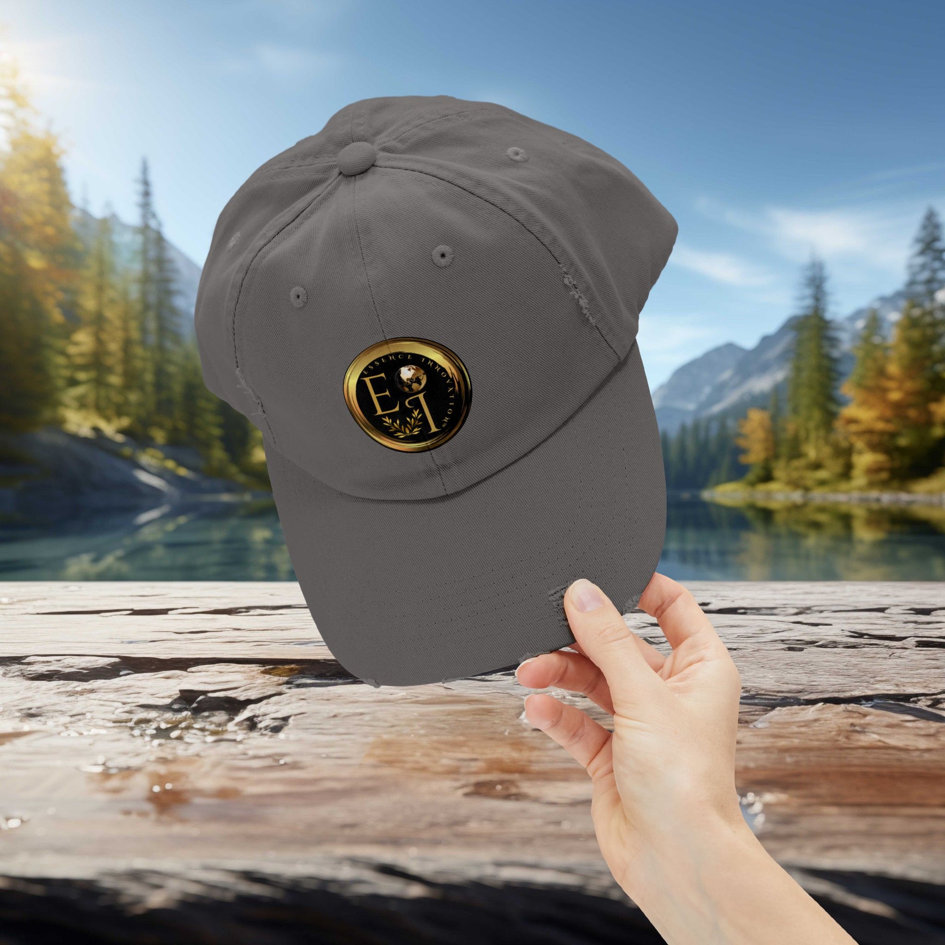 Gray Essence Innovation cap with a logo held by a hand against a scenic background of trees and water.