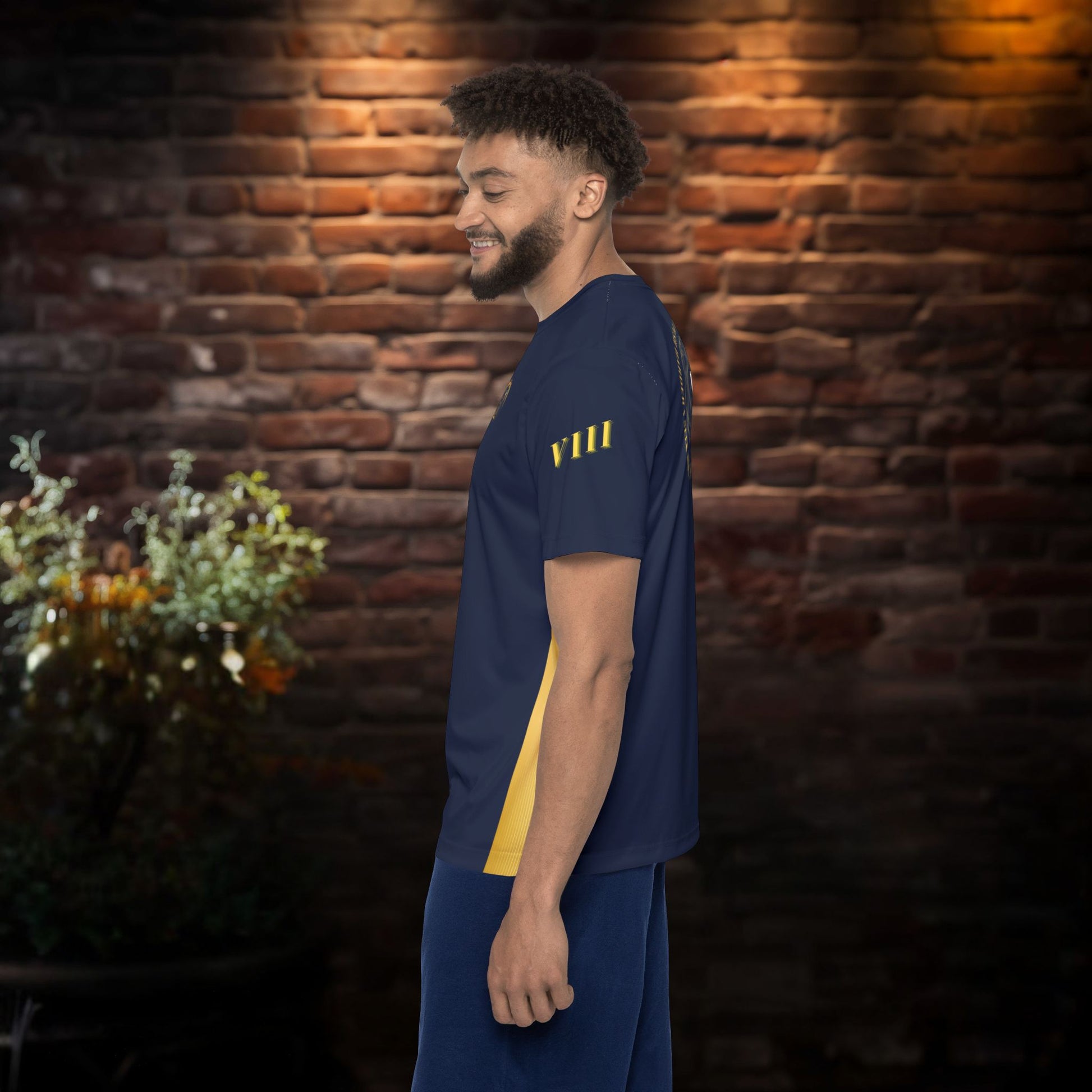Man wearing a navy blue t-shirt with yellow text standing against a brick wall.