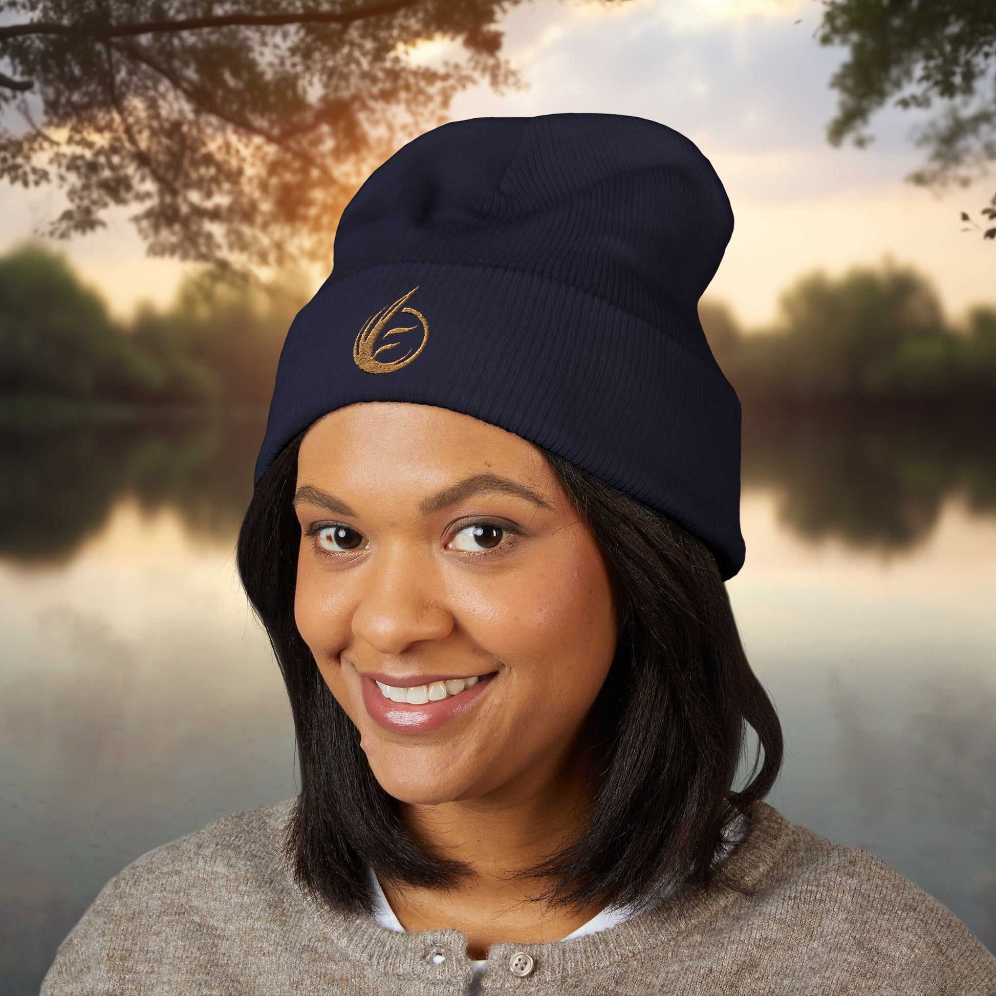 Person wearing a navy beanie with a EssenceInnoCreate logo, standing outdoors by a body of water.