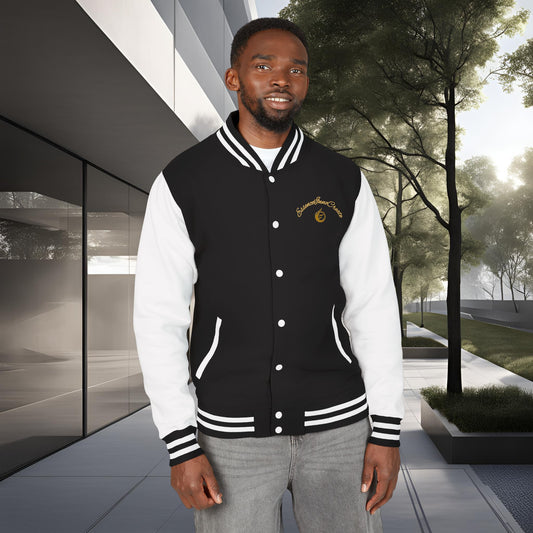 Man wearing a black and white EssenceInnoCreate varsity jacket standing outdoors with modern building and trees in the background