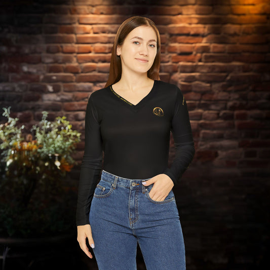 Woman wearing a black Essence Innovation Seek More long-sleeve top and blue jeans against a brick wall.