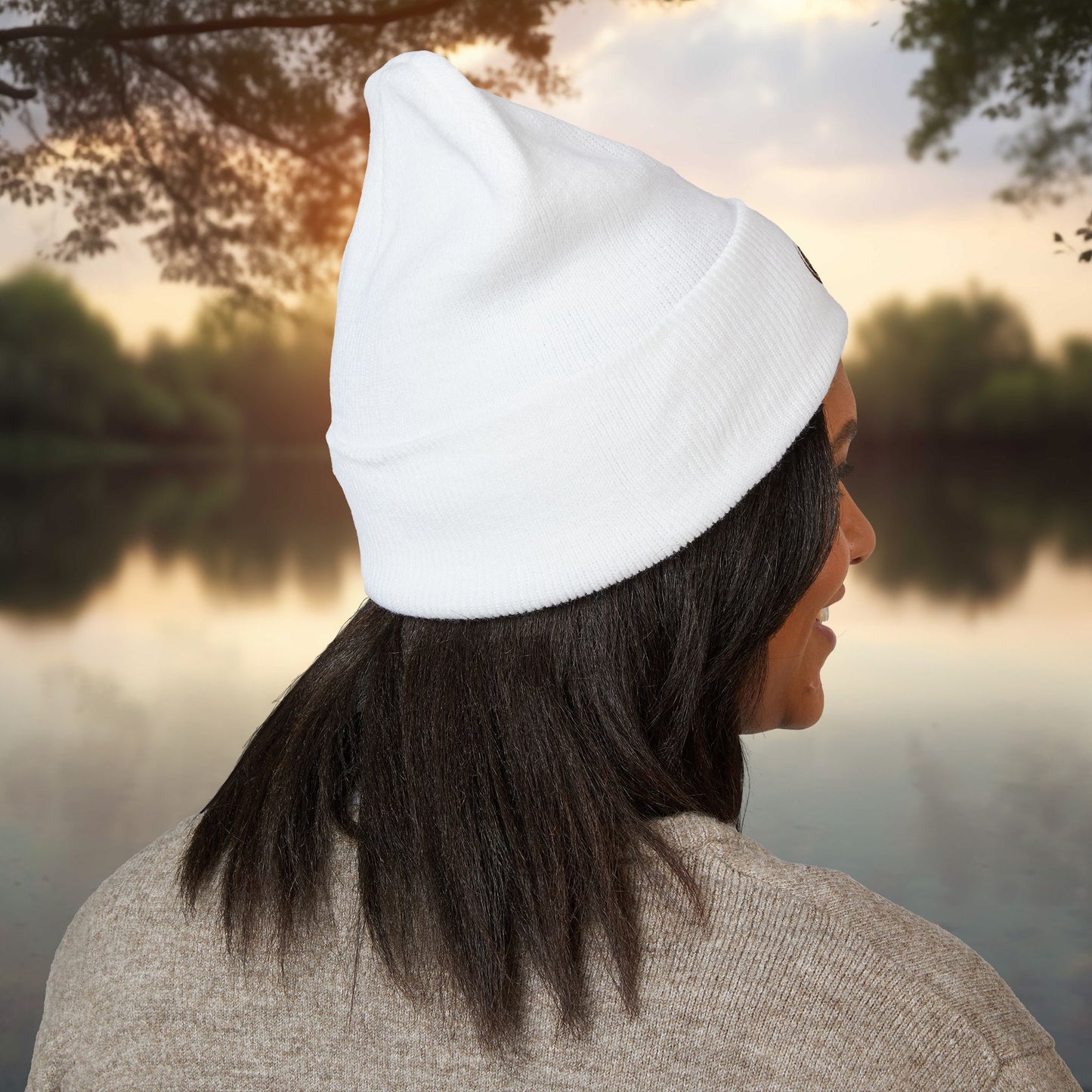 Person wearing a white EssenceInnoCreate beanie and looking at a lake during sunset.