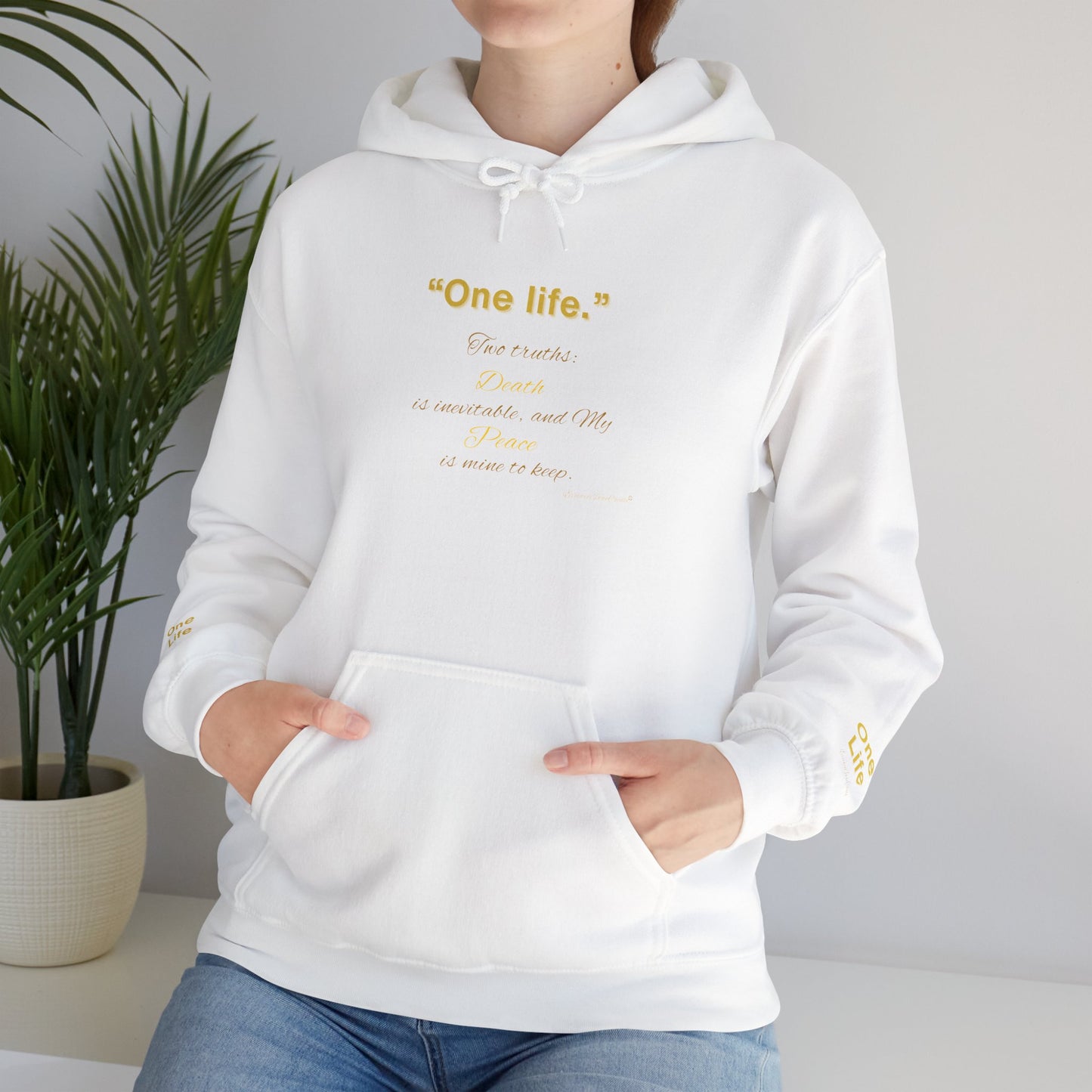 Person wearing a white Essence Innovation 'One Life' hoodie with colorful text and design, standing against a neutral background with a plant.