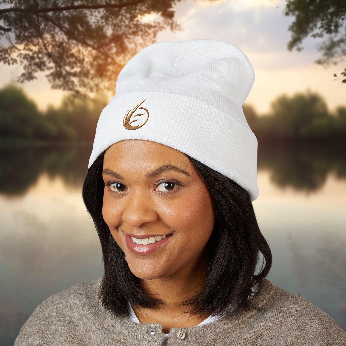 Person wearing a white beanie with a EssenceInnoCreate logo, standing outdoors by a body of water.