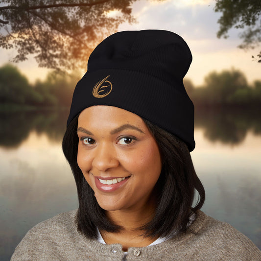 Person wearing a black beanie with a EssenceInnoCreate logo, standing outdoors with trees and water in the background