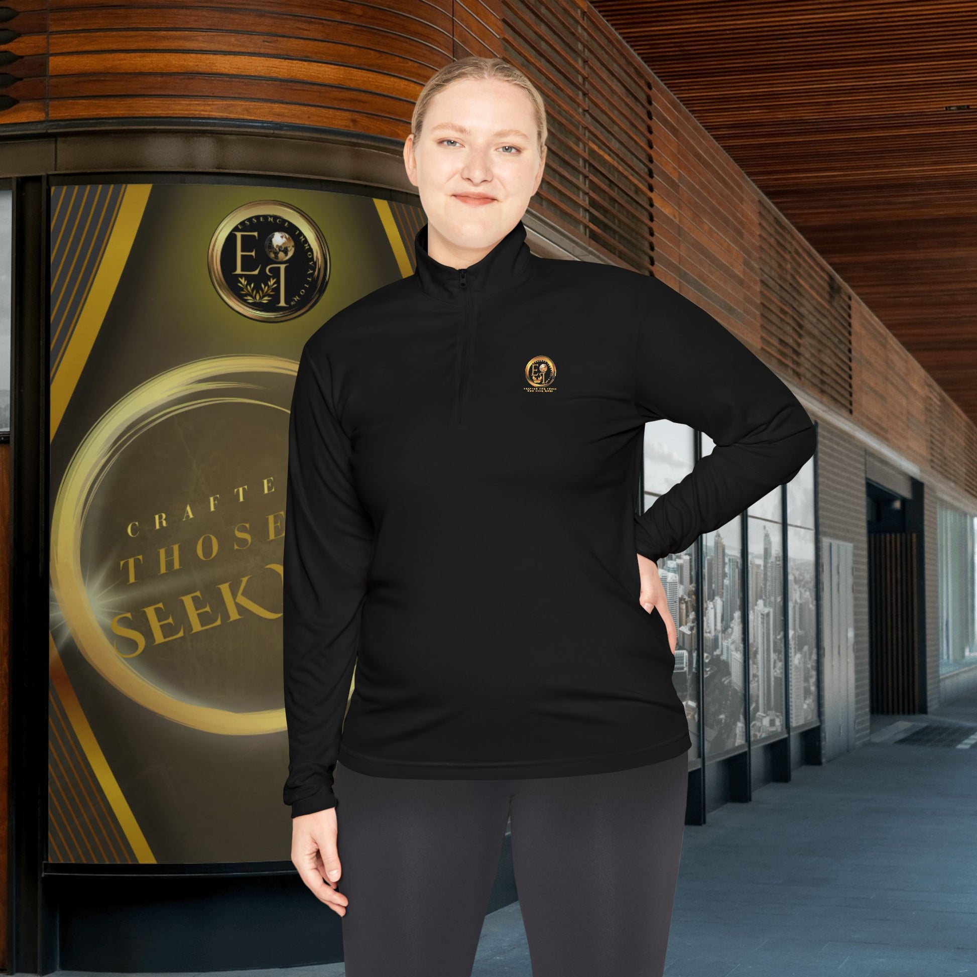 Person wearing a black Essence Innovation Seek More quarter-zip long sleeve with a logo in front of a building entrance