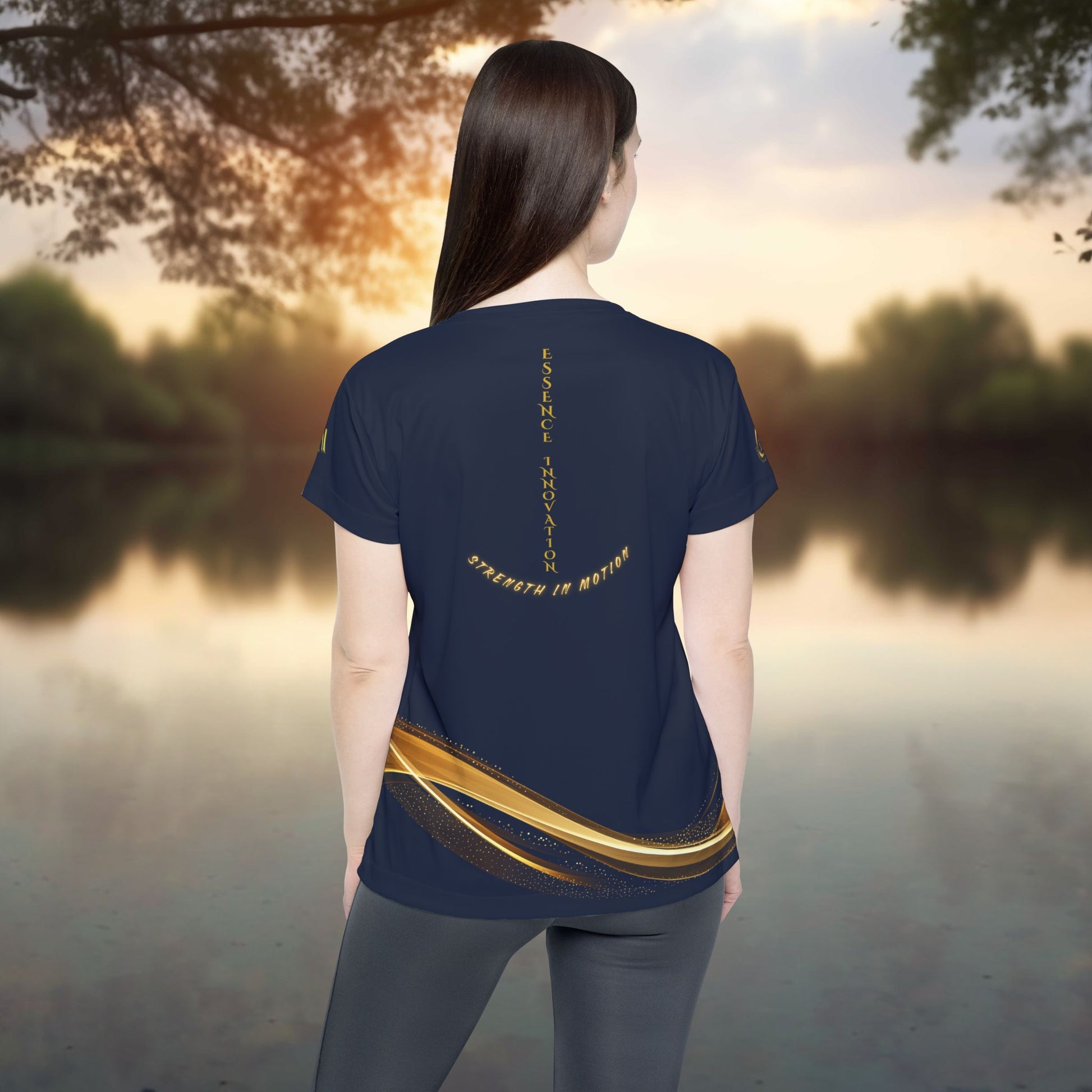 Person wearing a navy blue t-shirt with gold design and text, standing by a lake at sunset.