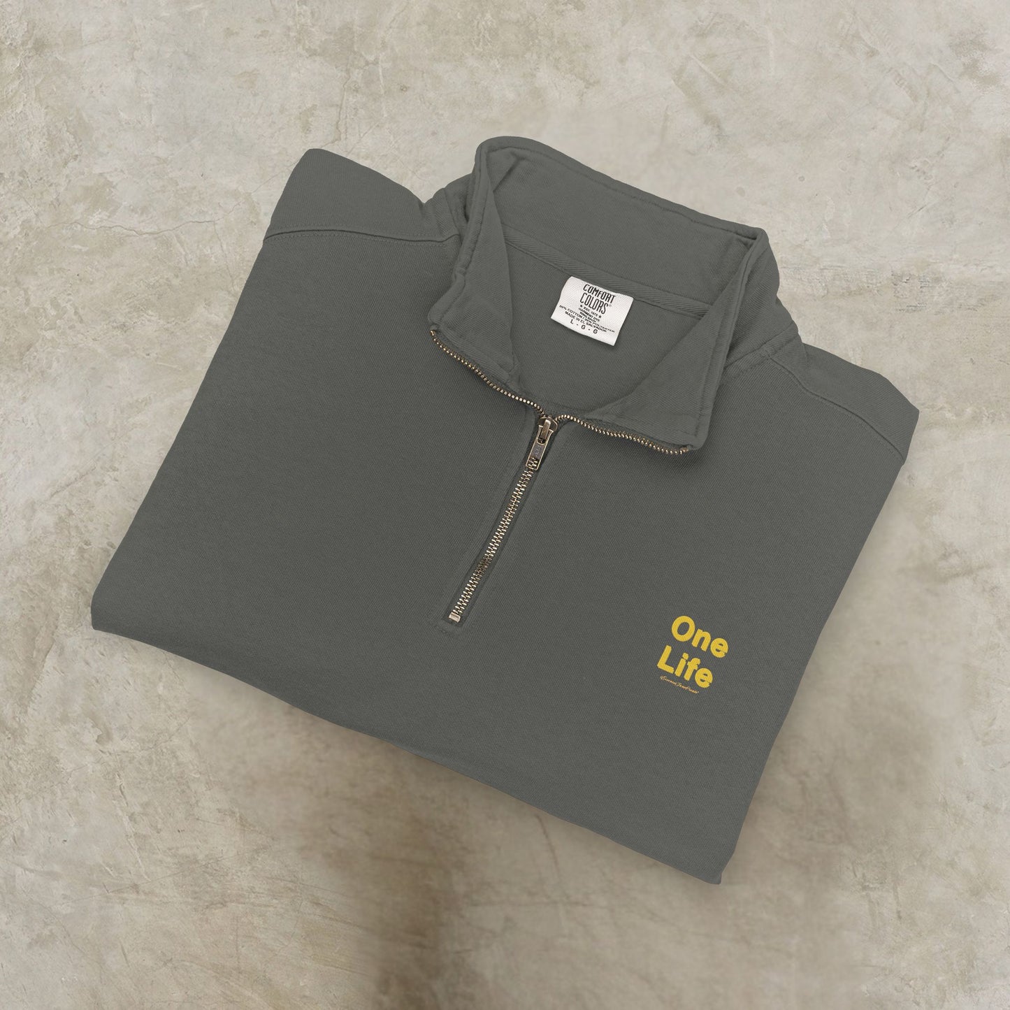 Folded gray pullover with 'One Life' text on a beige surface