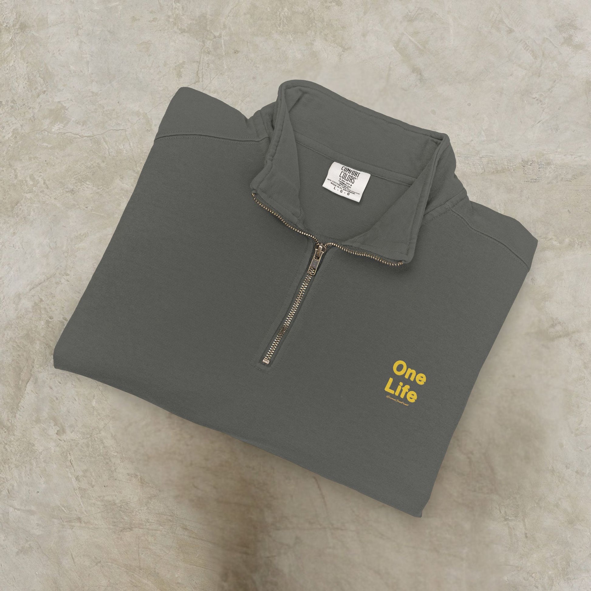 Folded gray pullover with 'One Life' text on a beige surface