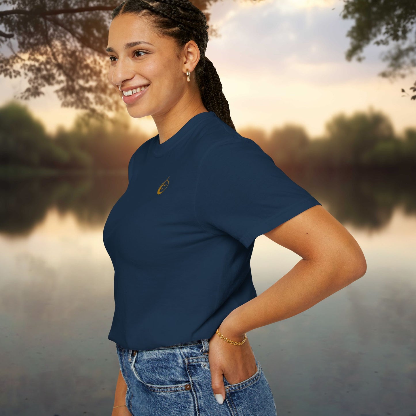 Woman wearing a blue t-shirt with 'EssenceInnoCreate' logo by a lake at sunset