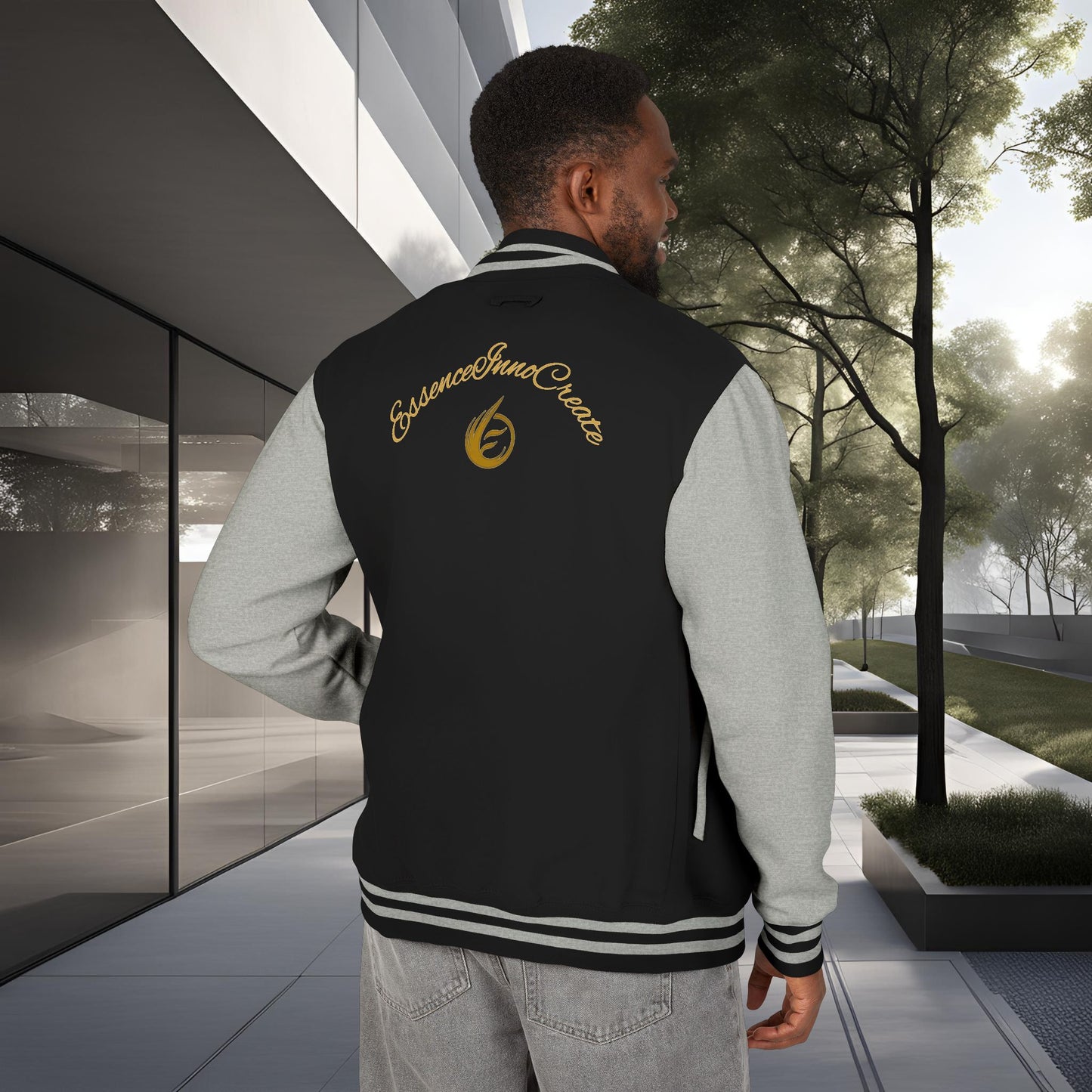 Man wearing a black letterman jacket with yellow 'EssenceInnoCreate' text standing in an outdoor setting.