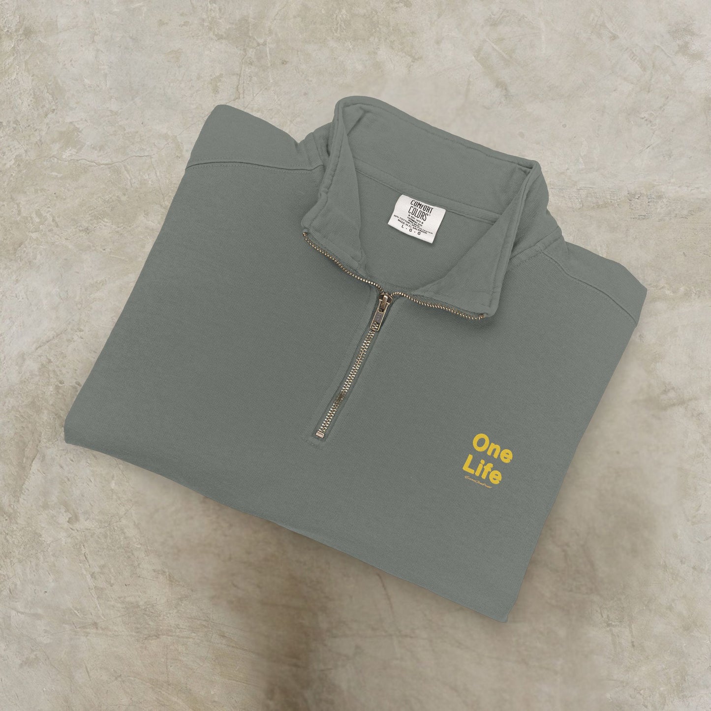 Folded gray pullover with 'One Life' text on a beige surface