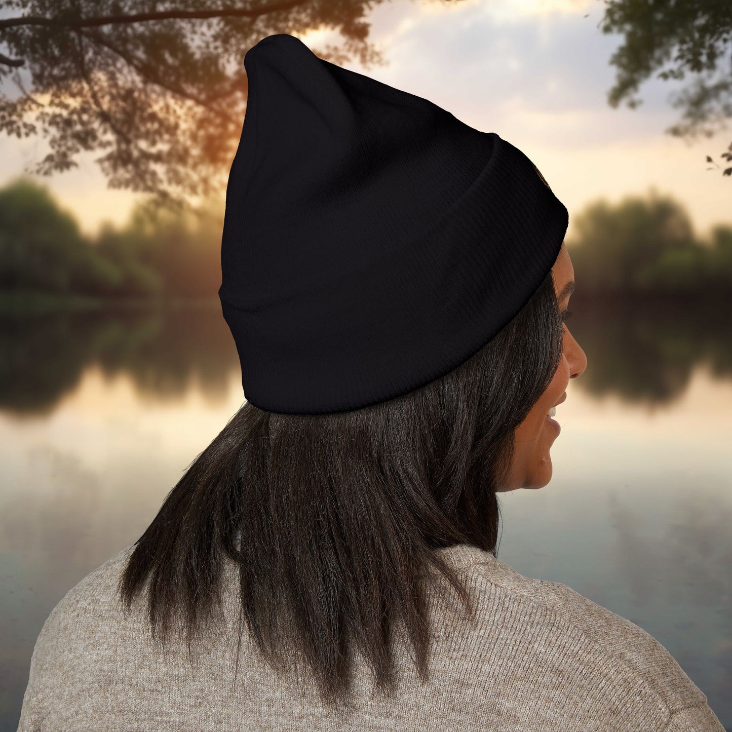 Person wearing a black EssenceInnoCreate beanie looking over a lake with trees in the background