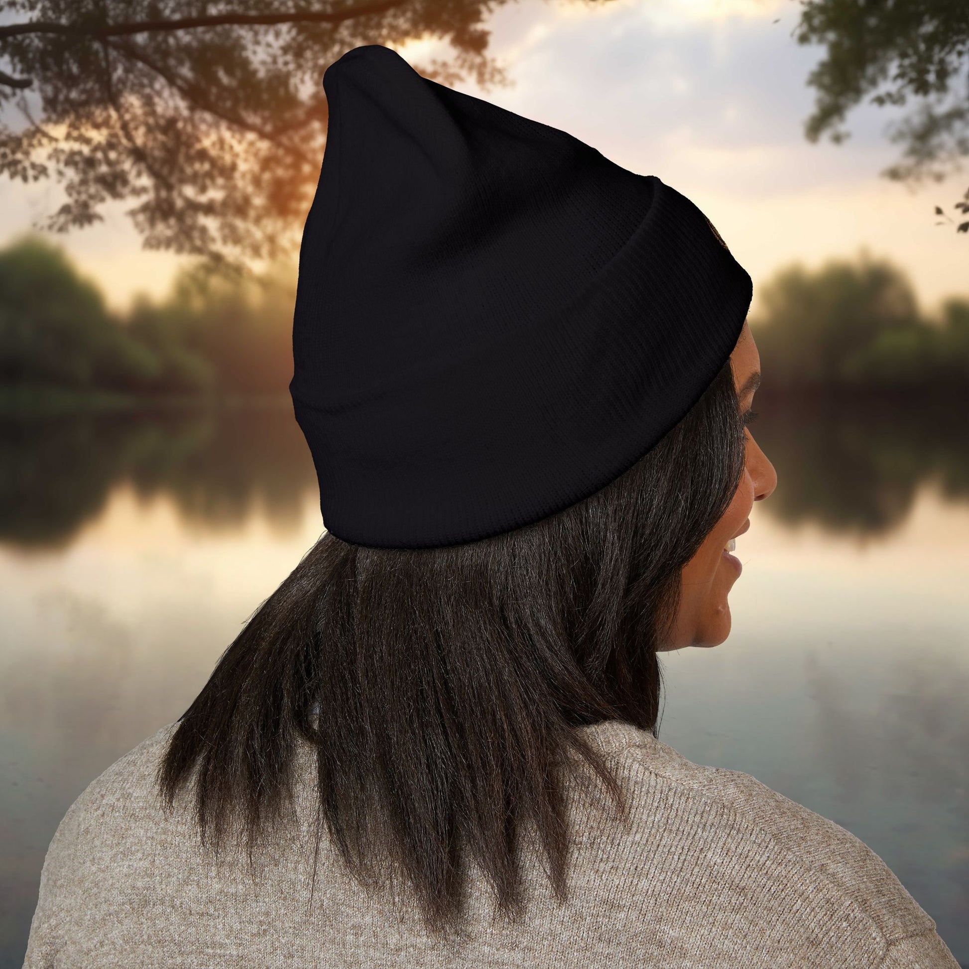 Person wearing a black EssenceInnoCreate beanie looking over a lake with trees in the background