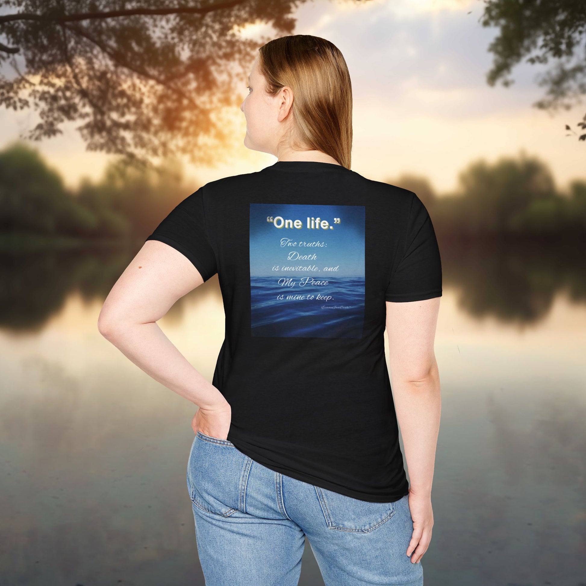 Person wearing a black t-shirt with a blue graphic and One Life text by a lake at sunset