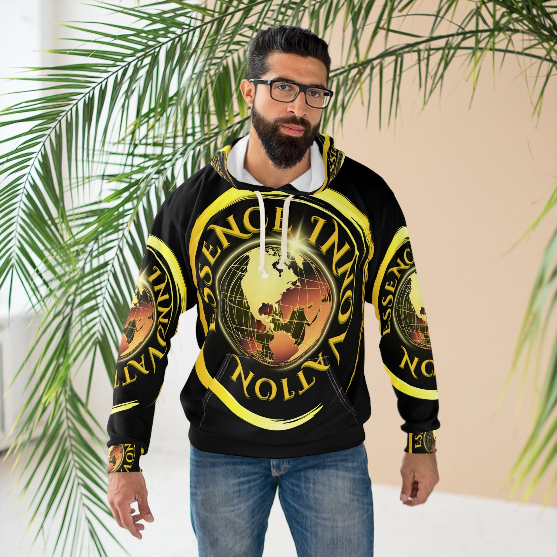 Man wearing a black hoodie with yellow graphics and text, standing in front of green plants.