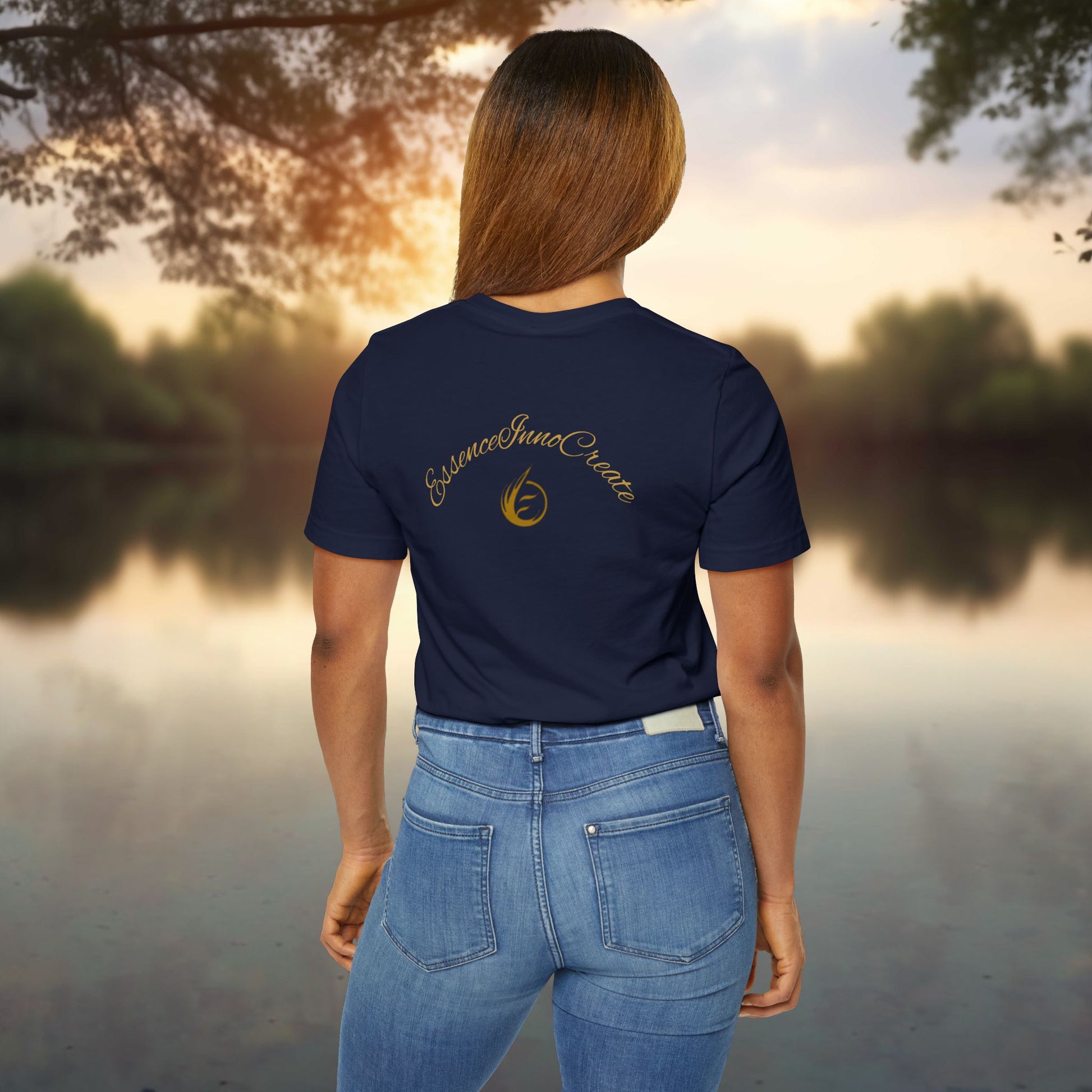 Person wearing a navy blue t-shirt with 'EssenceInnoCreate' logo standing by a lake at sunset.