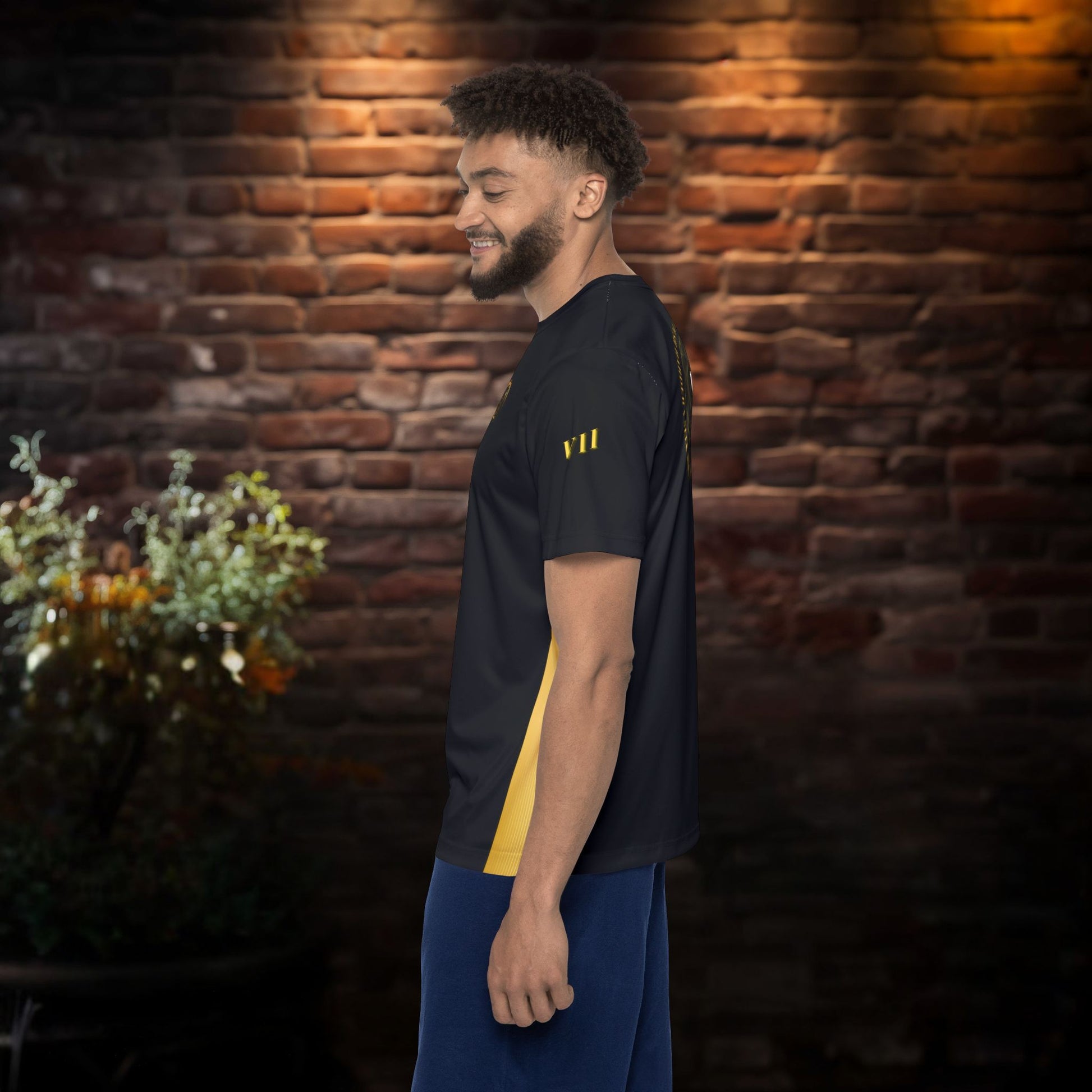 Man wearing a black t-shirt with yellow text standing against a brick wall.