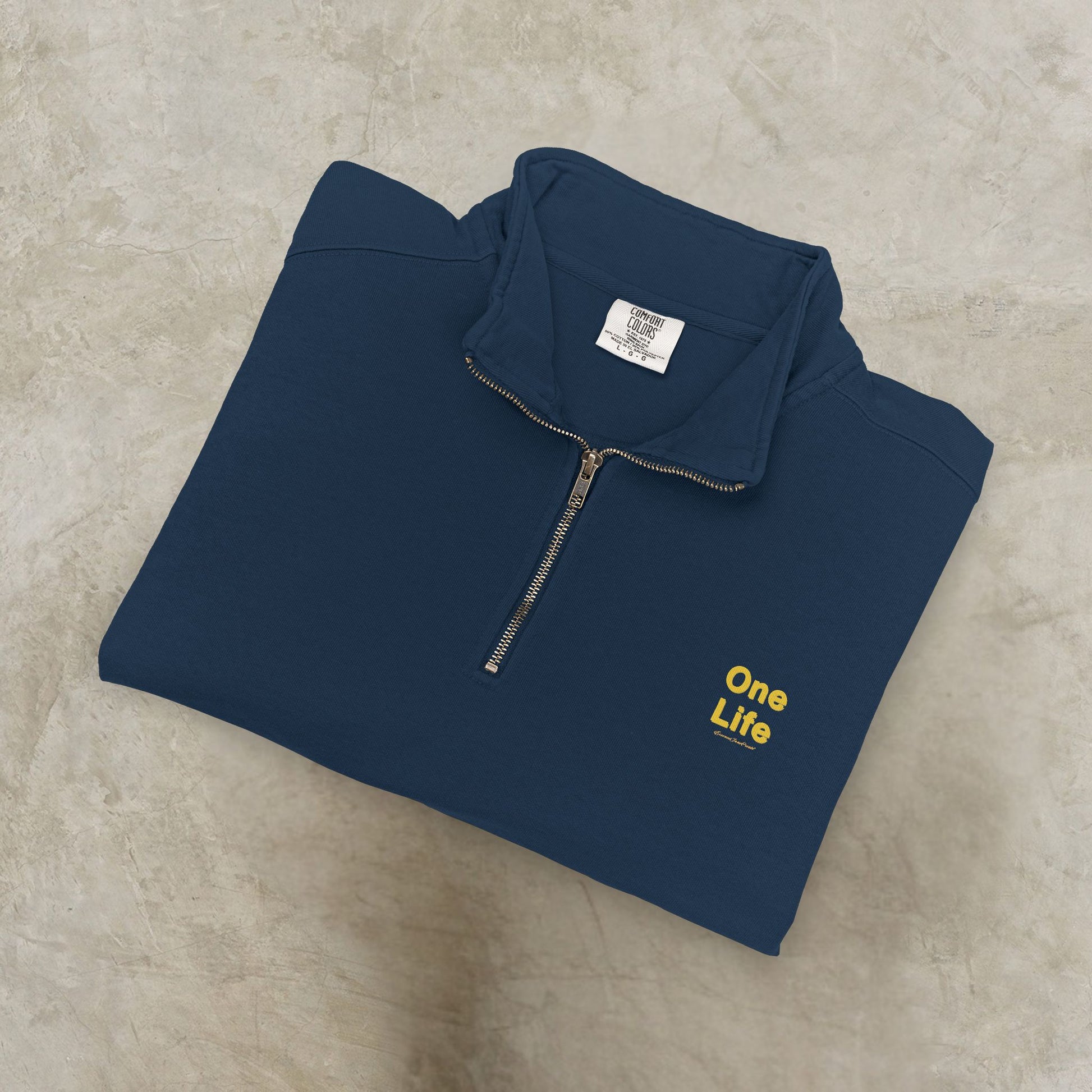 Folded navy blue pullover with 'One Life' text on a beige surface