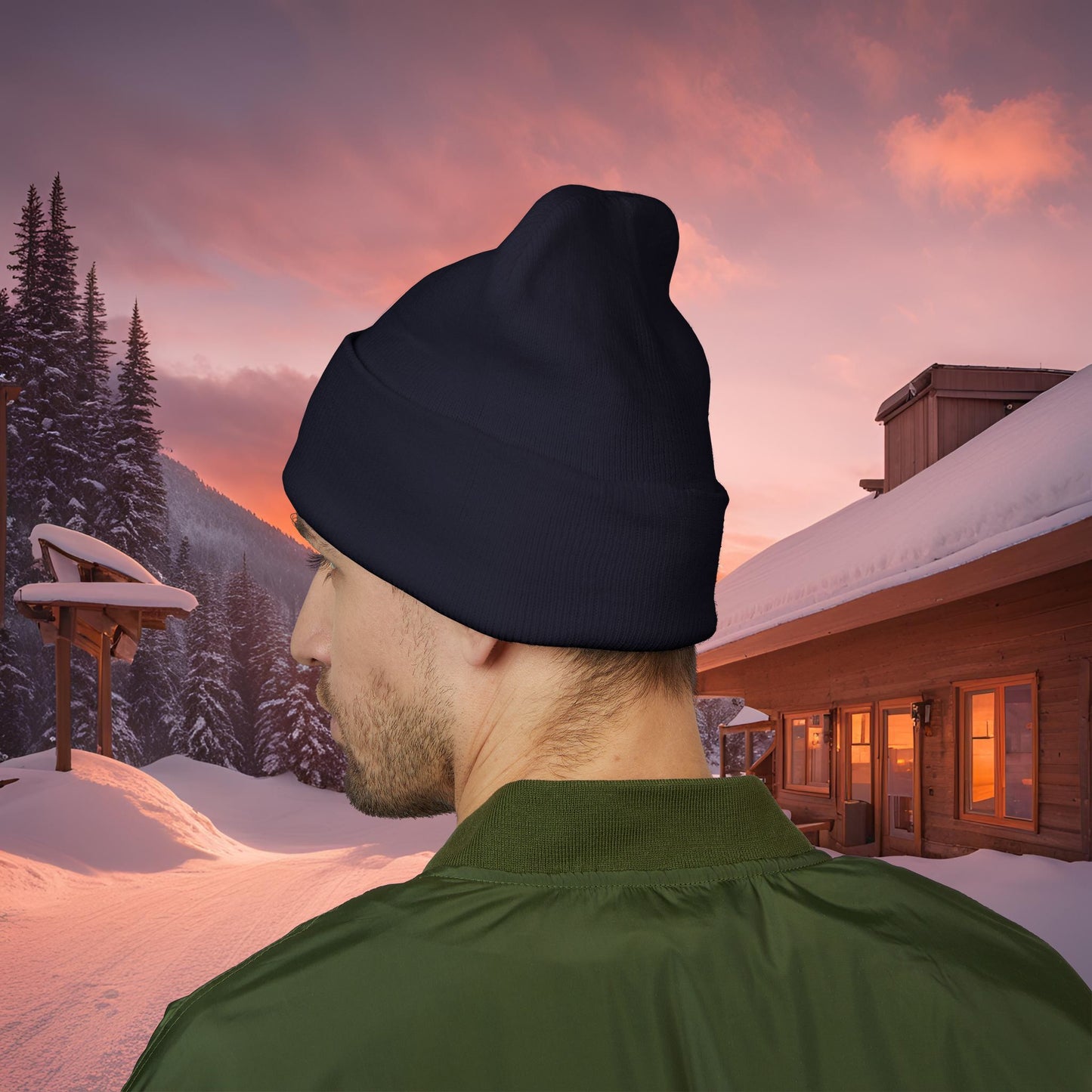 Person wearing a black EssenceInnoCreate beanie and green jacket in a snowy landscape with a cabin and sunset.