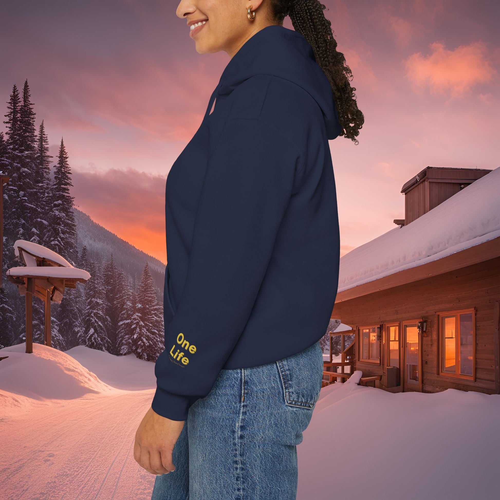 Person wearing a navy blue Essence Innovation sweatshirt with 'One Life' text in a snowy landscape with a cabin and sunset.
