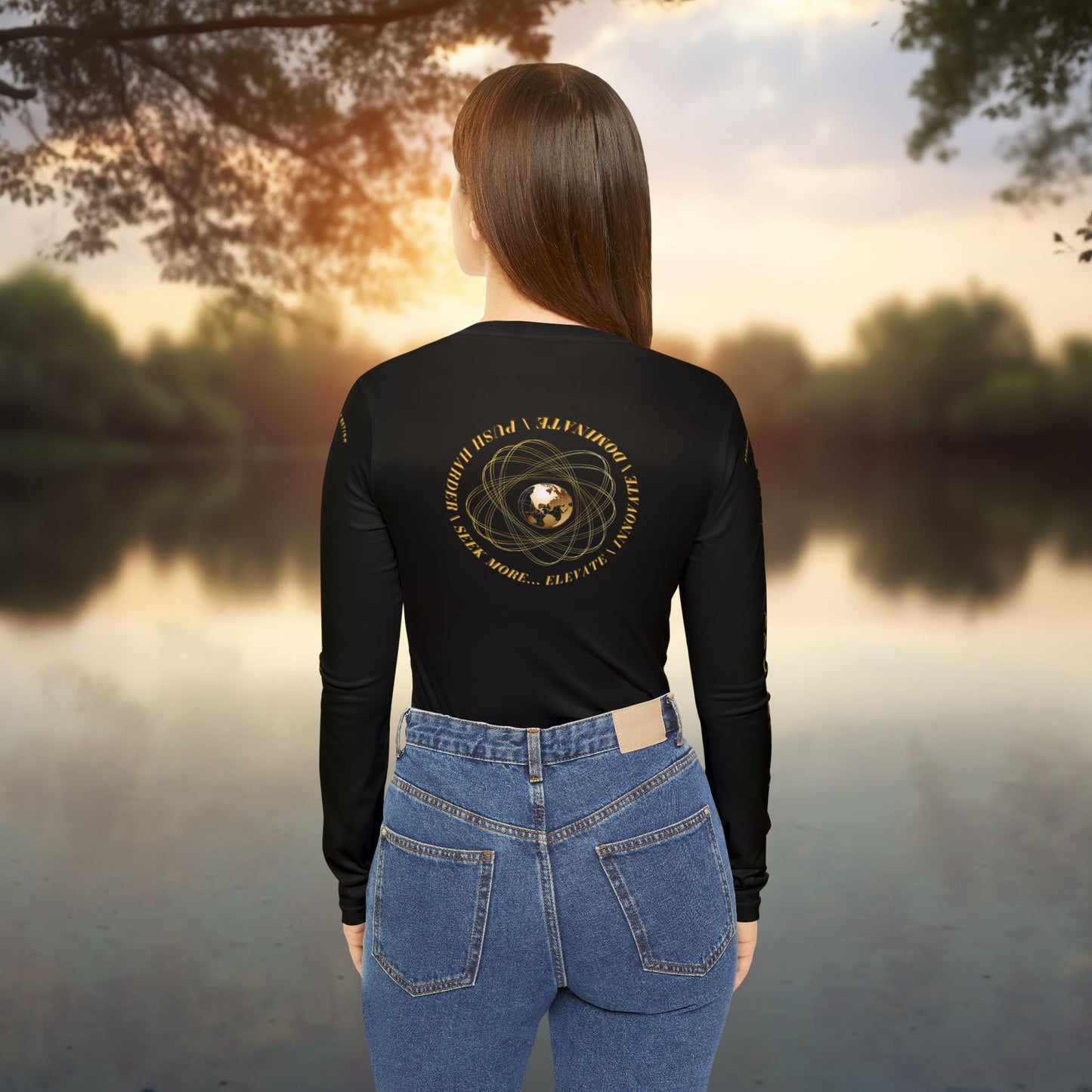 Person wearing a black Essence Innovation Seek More long-sleeve shirt with a design on the back, standing by a lake at sunset.