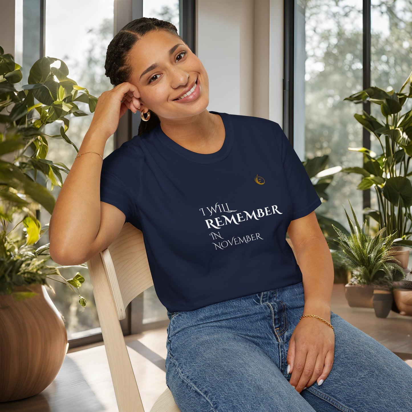 Woman wearing a navy blue EssenceInnoCreate Quiet Resolve t-shirt with text, sitting indoors with plants around.