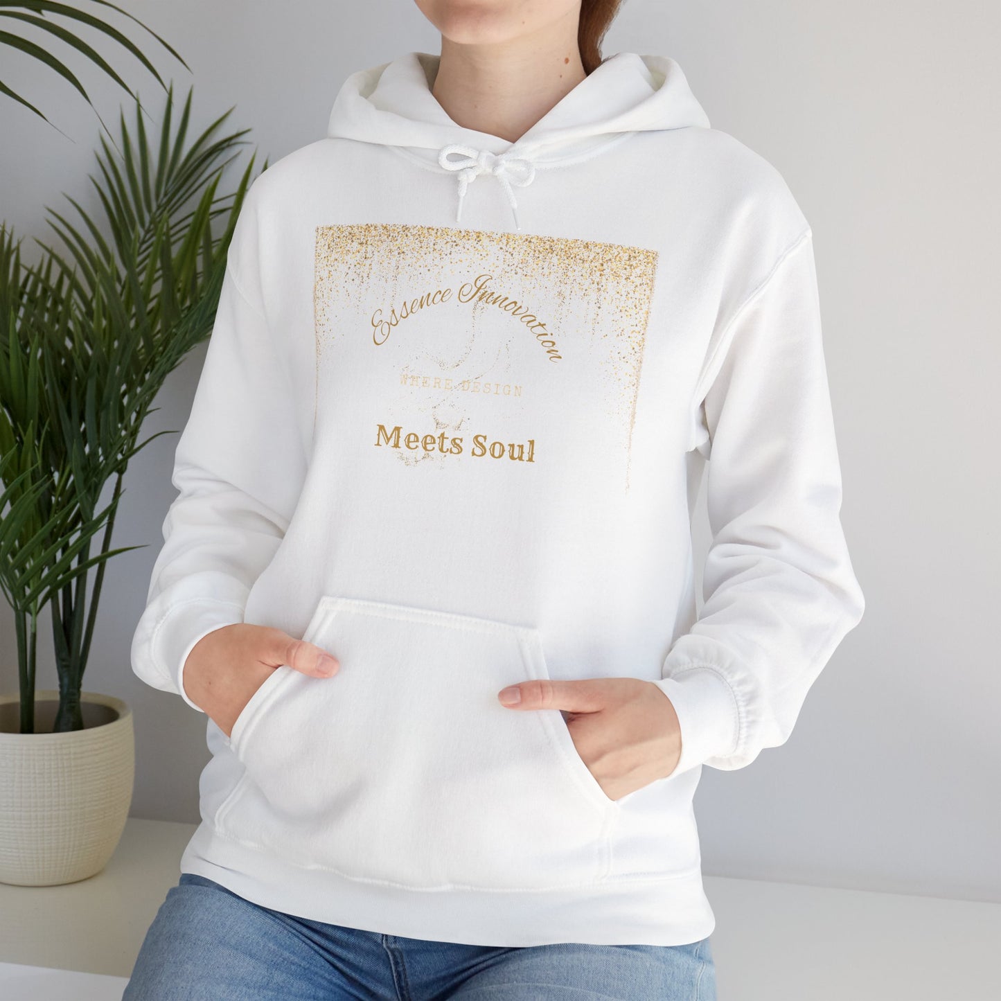 White hoodie with gold Essence Innovation 'Design Meets Soul' text worn by a person, against a neutral background with a plant.